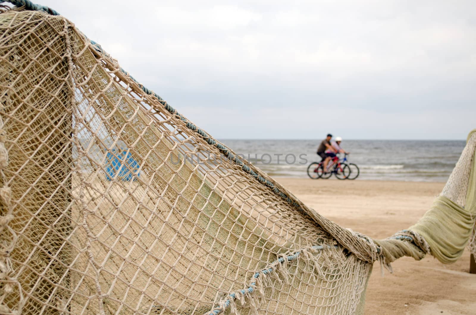 Beach fence decorated with net and cyclists going on sea shore coastline.