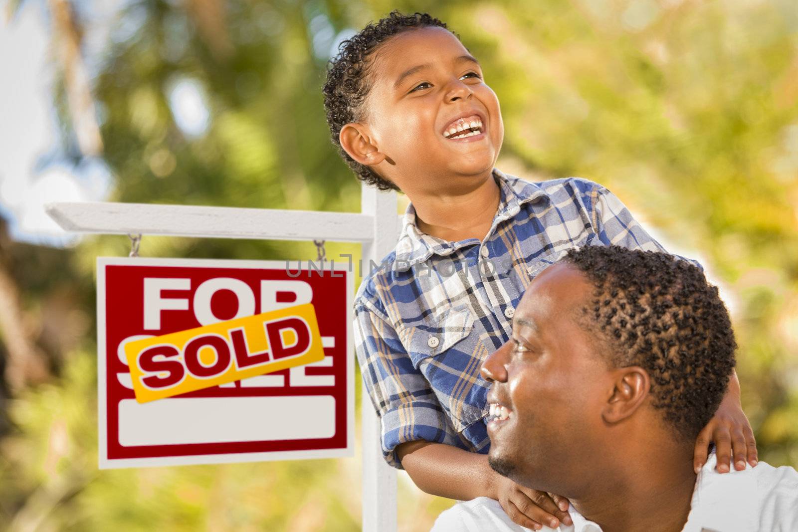 Happy African American Father and Mixed Race Son in Front of Sold Real Estate Sign.