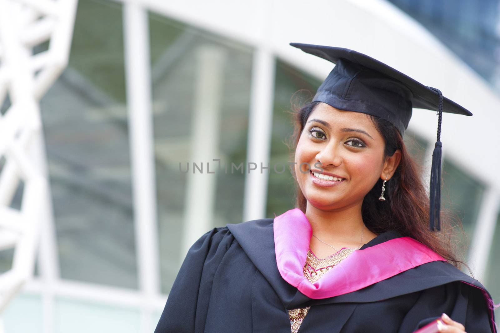 Stock image of Indian female graduate student standing in front school buiding