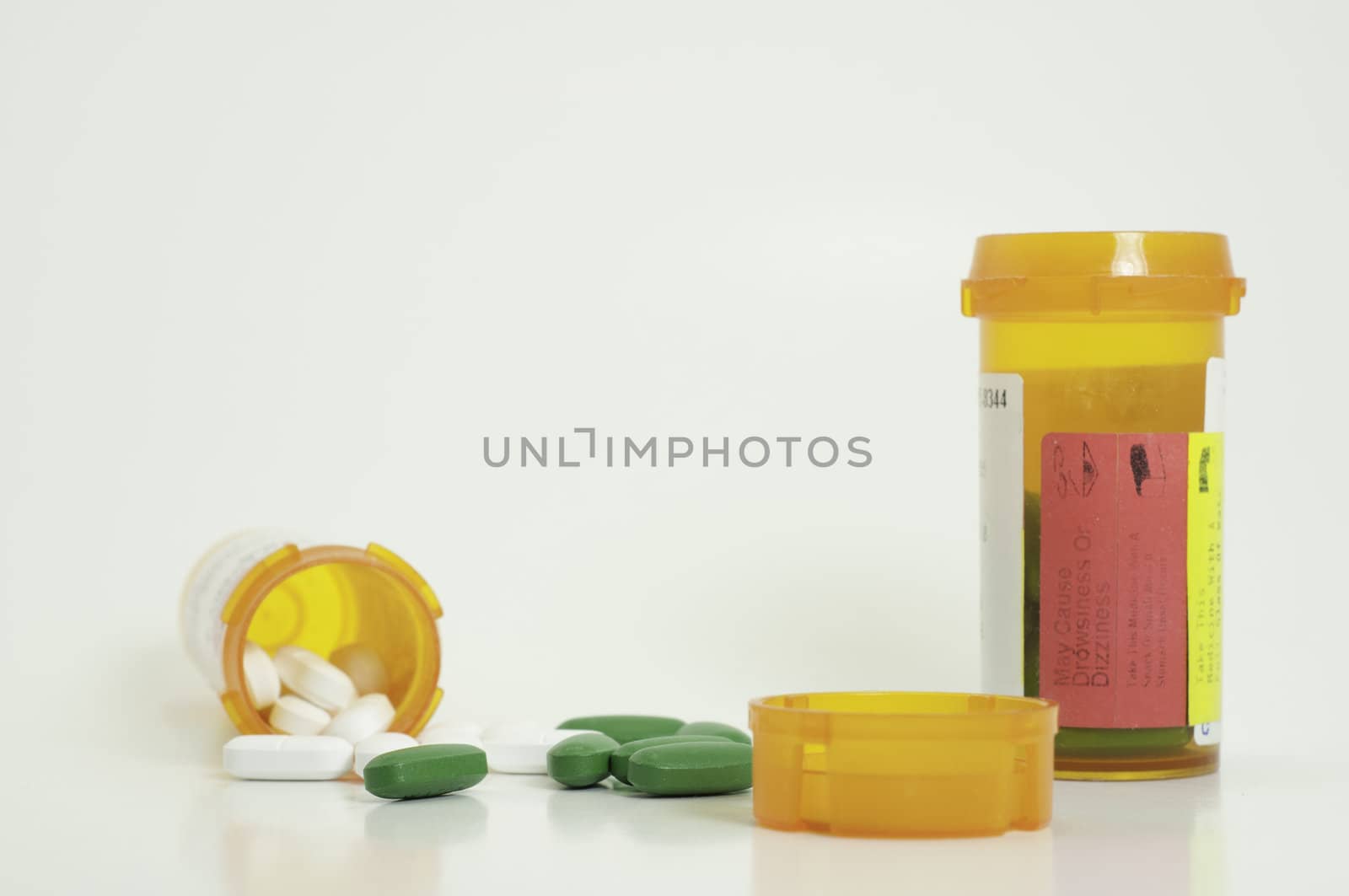 spilled white and green prescription pills with two bottles and a lid in foreground