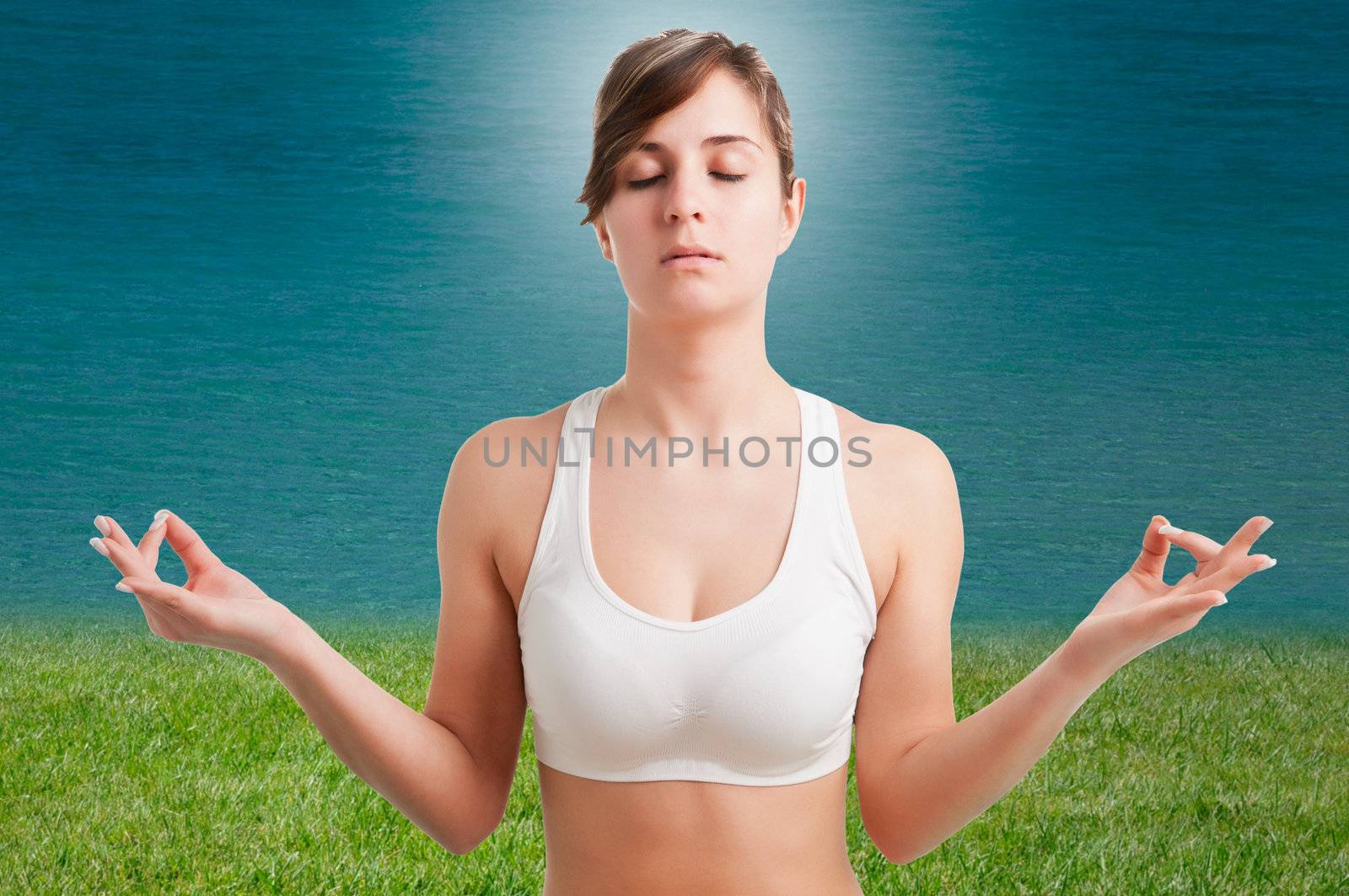 Woman doing yoga on grass, next to the sea, with a sun flare behind her head