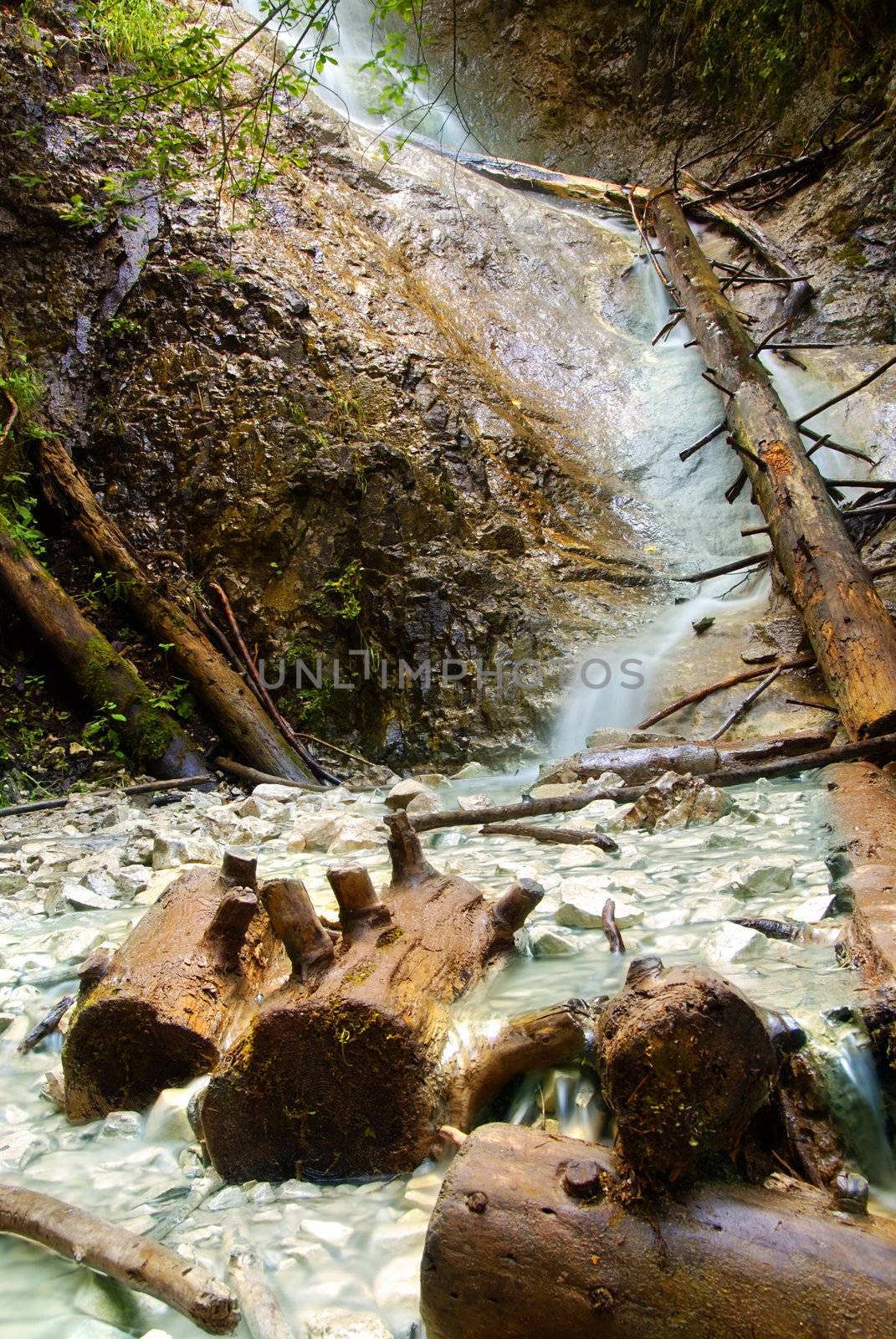 One of the many crystal clear waterfalls in the Slovakian paradise natural park with wooden logs in the front