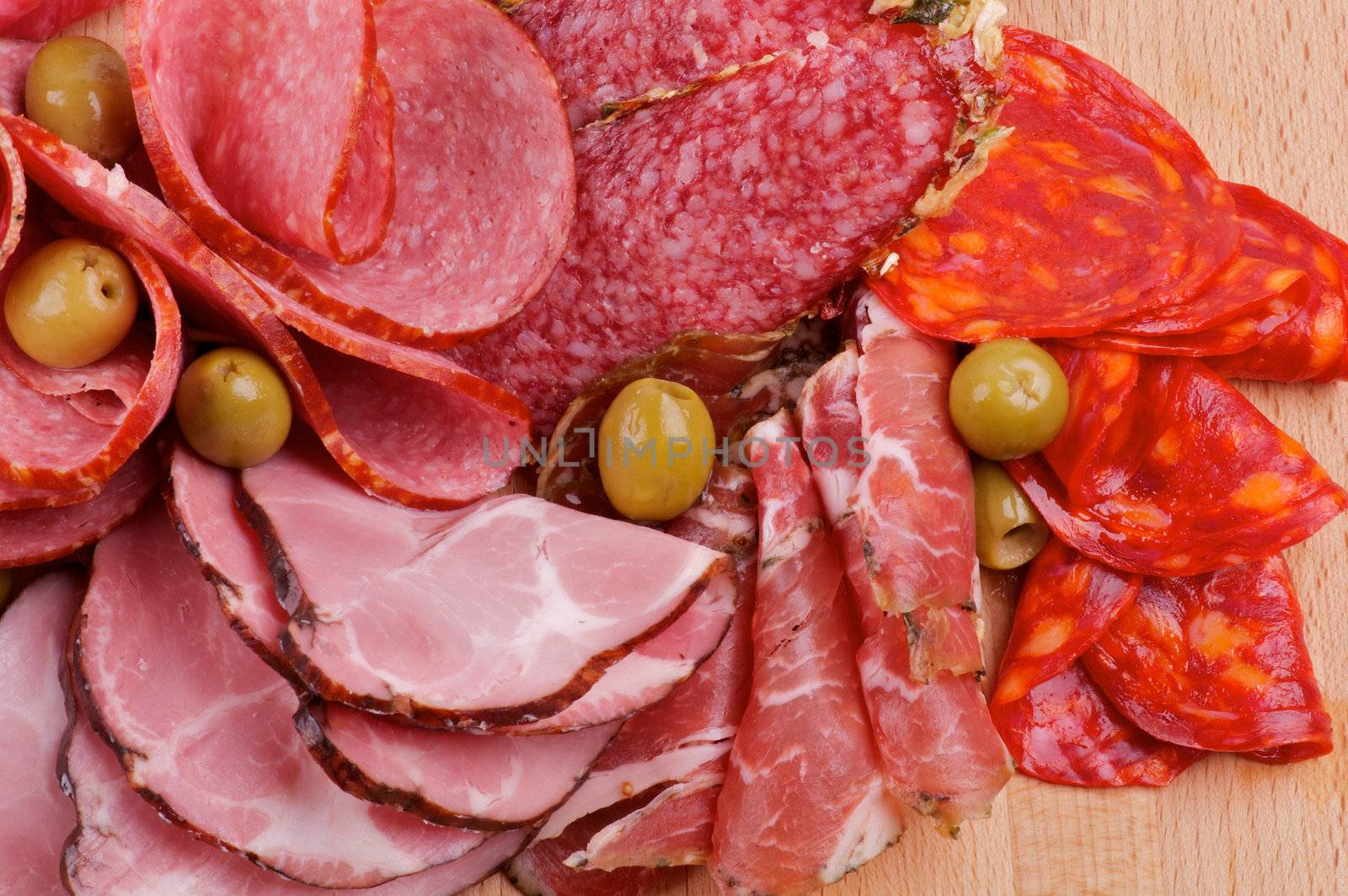 Arrangement of Meat delicatessen with Ham, Pepperoni, Chorizo and Olives close up on wooden backgound