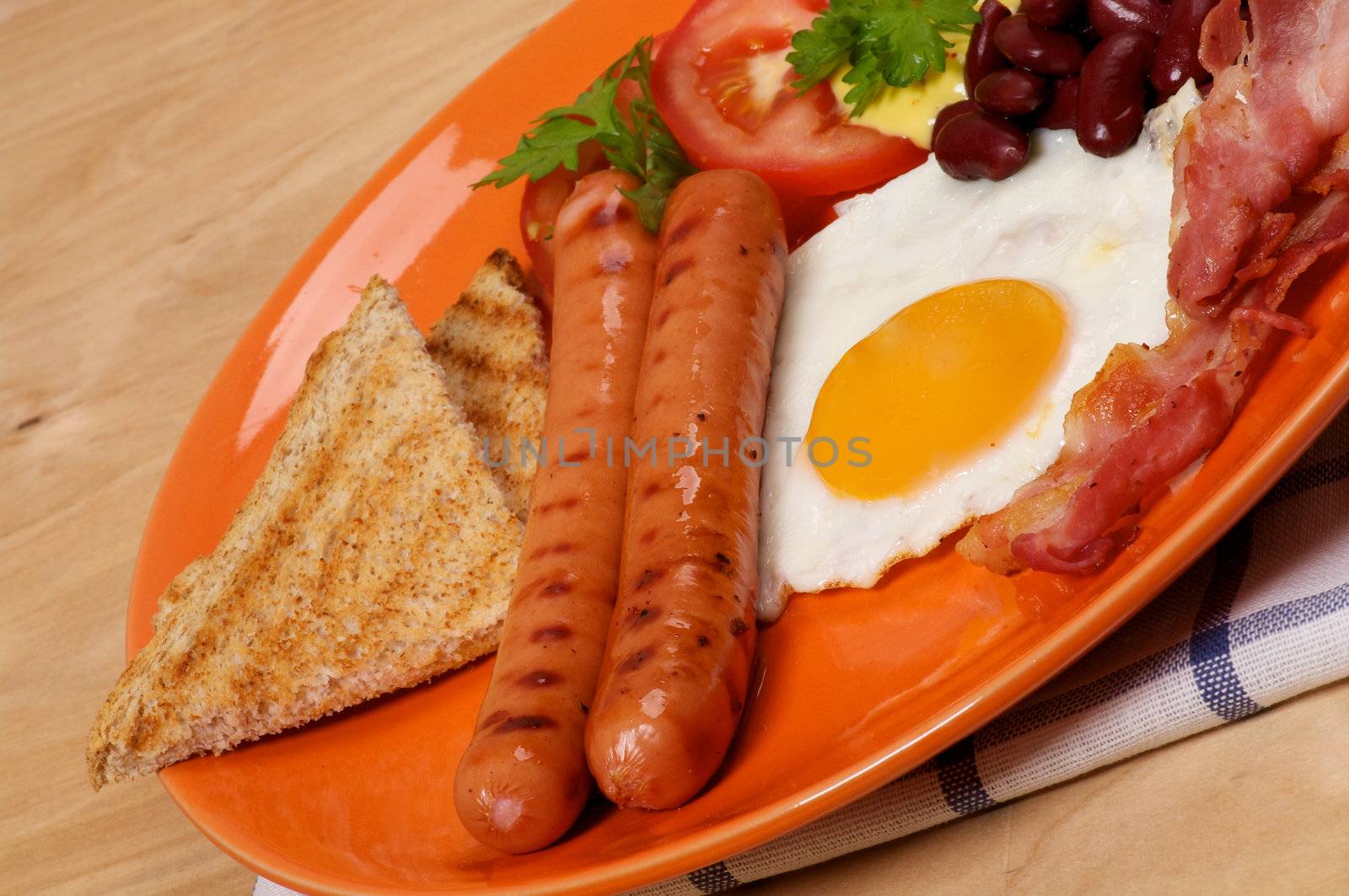 English Breakfast with Sausage, Bacon, Fried Eggs Sunny Side up, Beans, Tomato and Toasts close up on orange plate