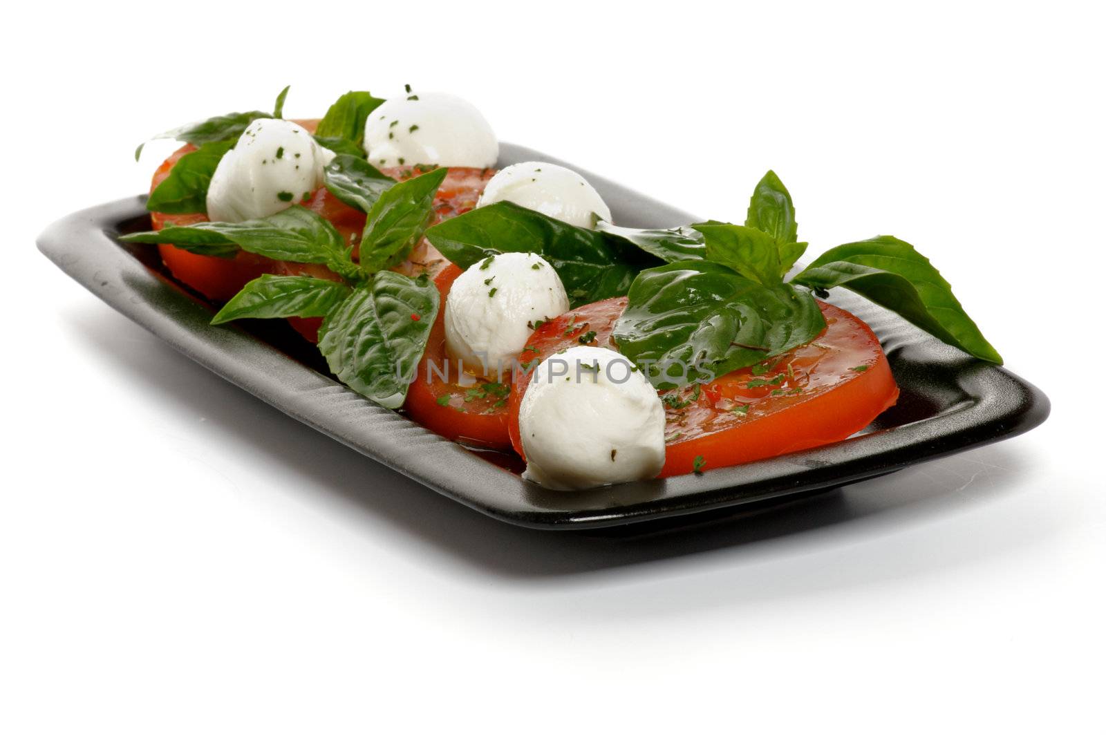 Italian Caprese Salad with Basil, Fresh Mozzarella, Tomatoes and Olive Oil on Black plate isolated on white background