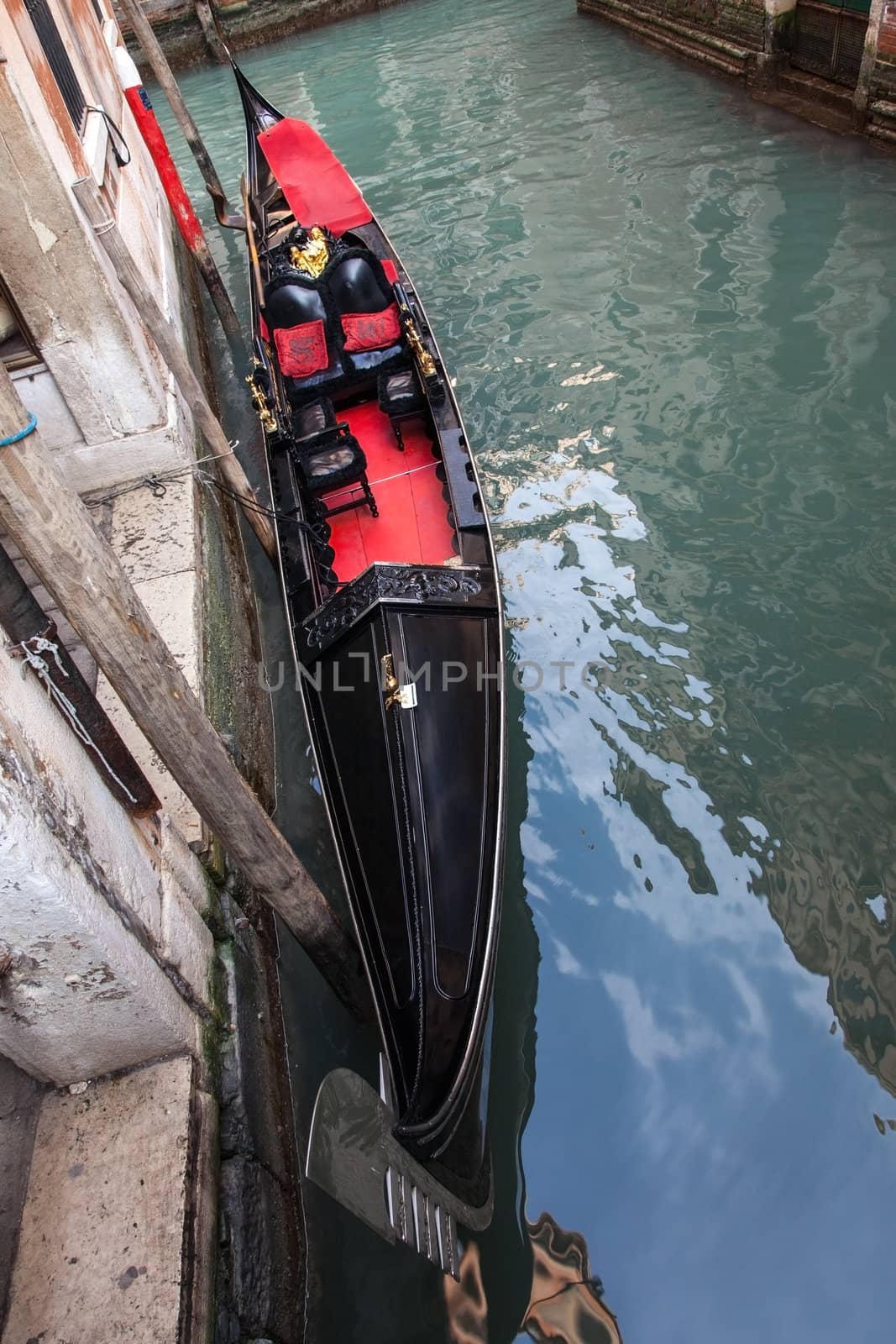 A gondola parked near a wall of a building on a Venetian canal.