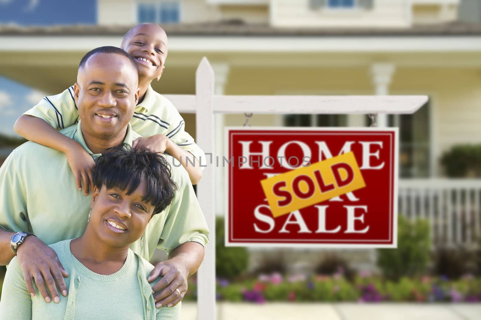 Happy African American Family In Front of Sold Real Estate Sign and House.