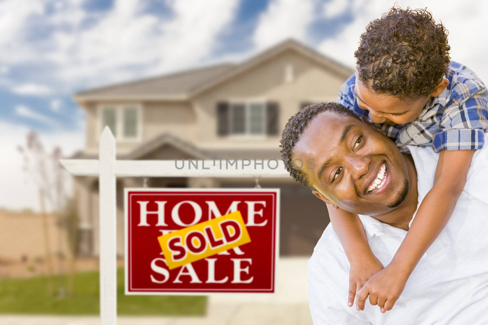 Happy Mixed Race Father and Son In Front of Sold Real Estate Sign and New House.