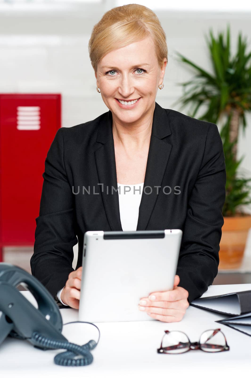 Cheerful businesswoman holding tablet pc and looking at camera