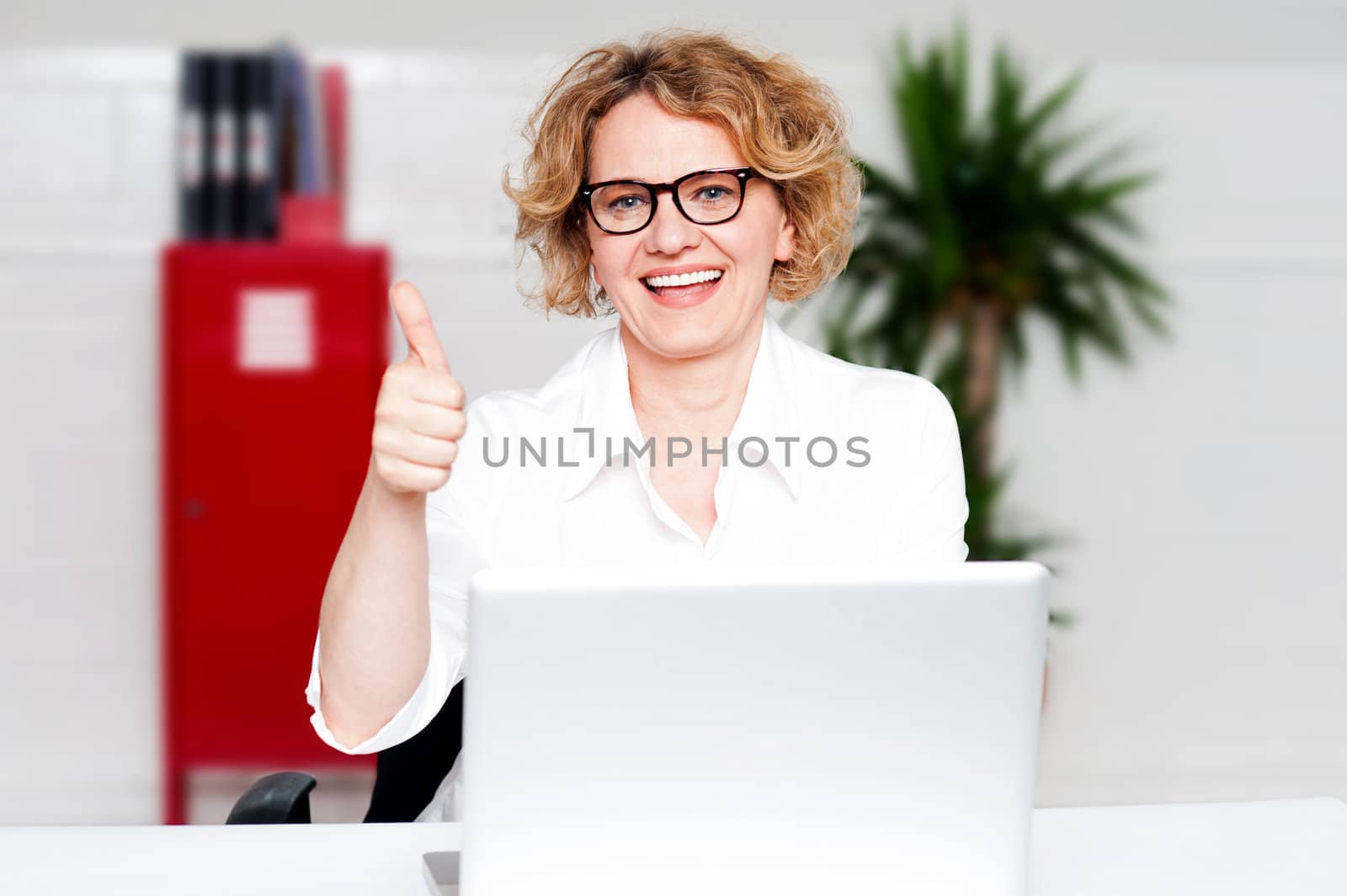 Successful businesswoman seated in office gesturing thumbs up to camera