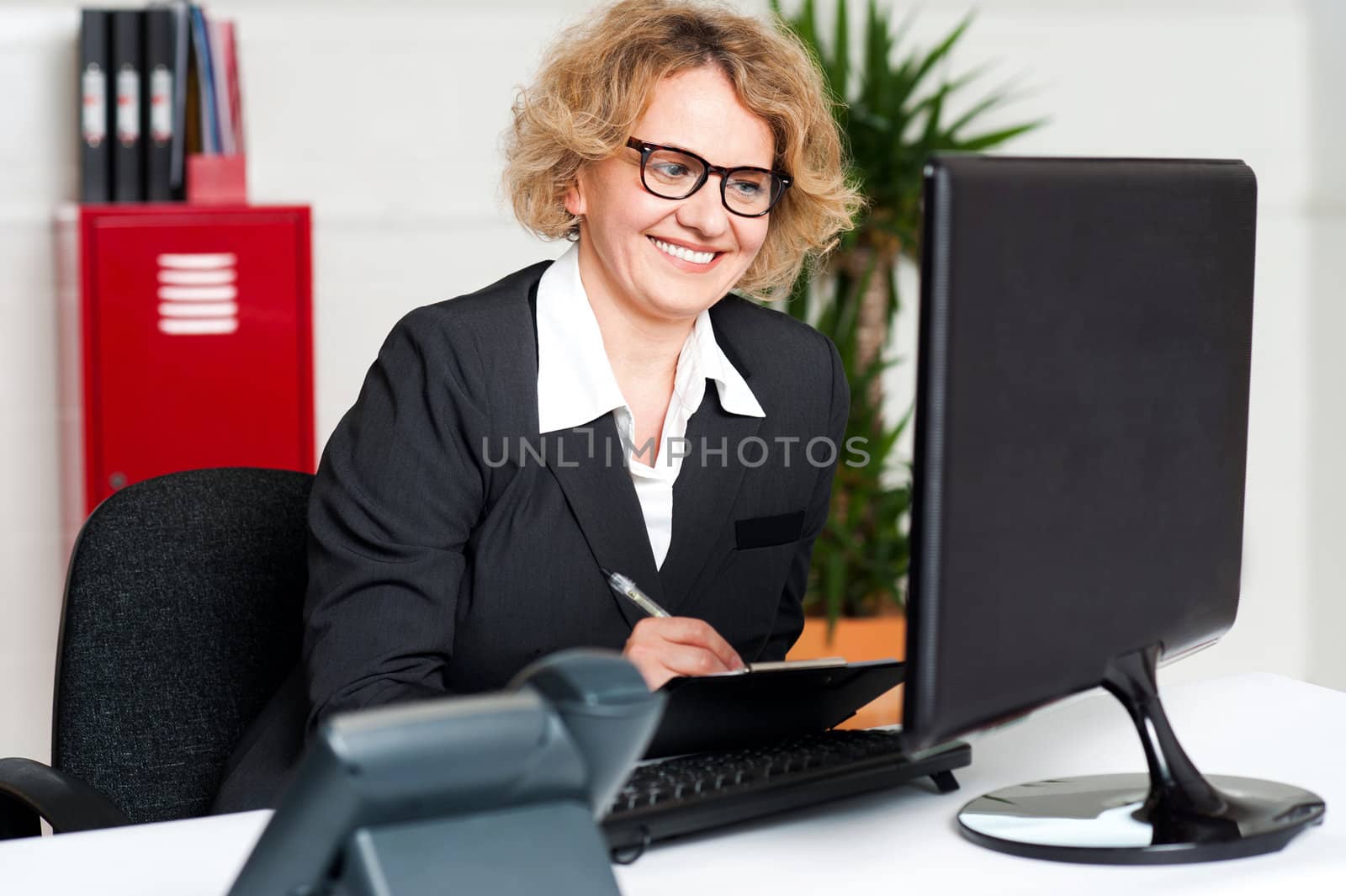 Female secretary wearing eyeglasses holding pen and looking at computer screen