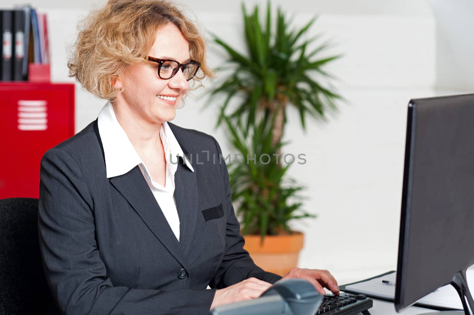 Aged woman in office wearing eyeglasses working on computer