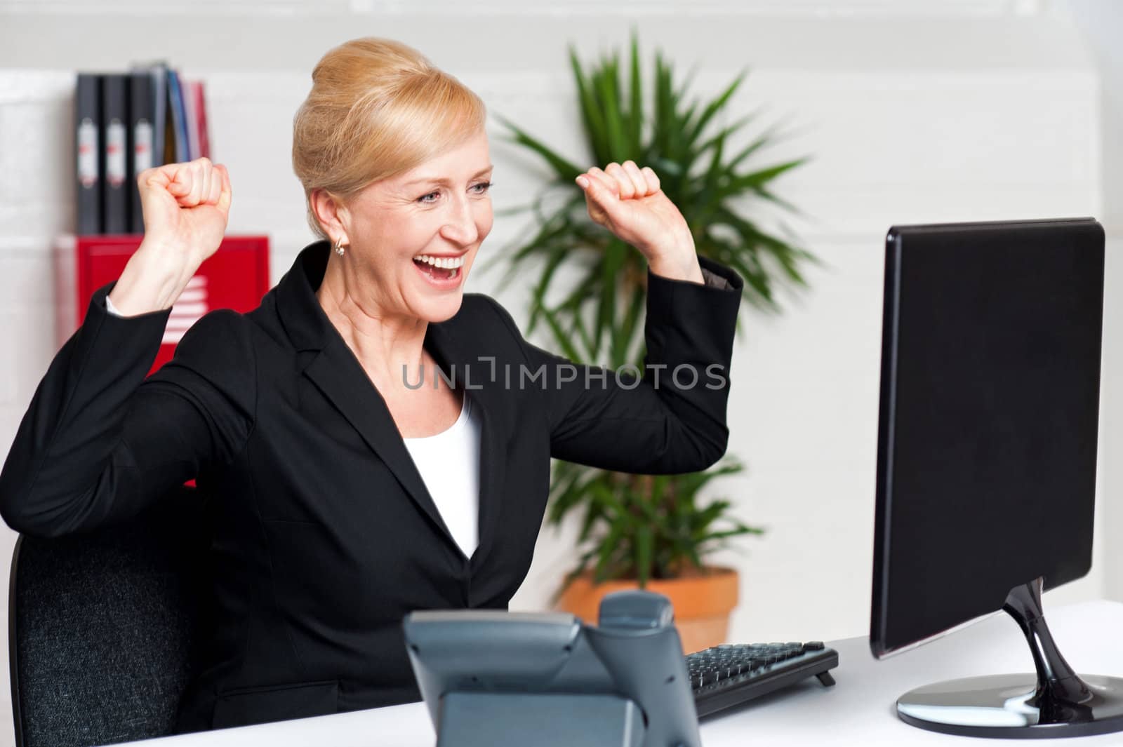 Excited corporate lady with raised arms looking at computer screen