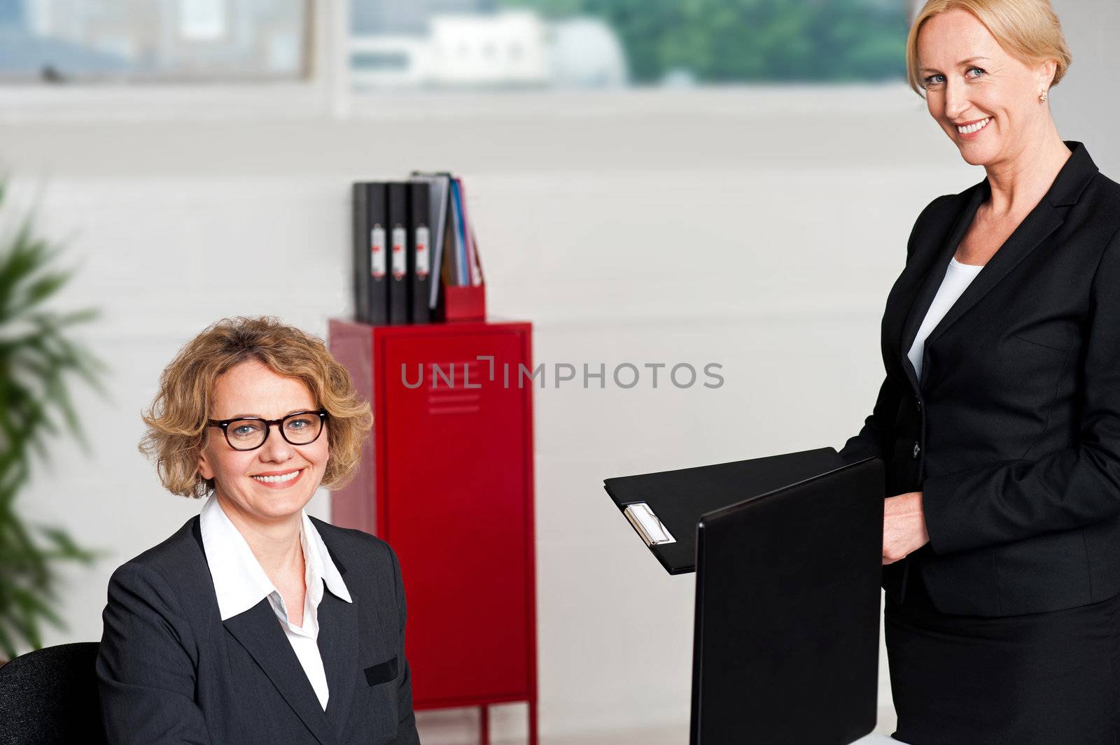 Woman handing over files to her female boss. Shot in office, indoors