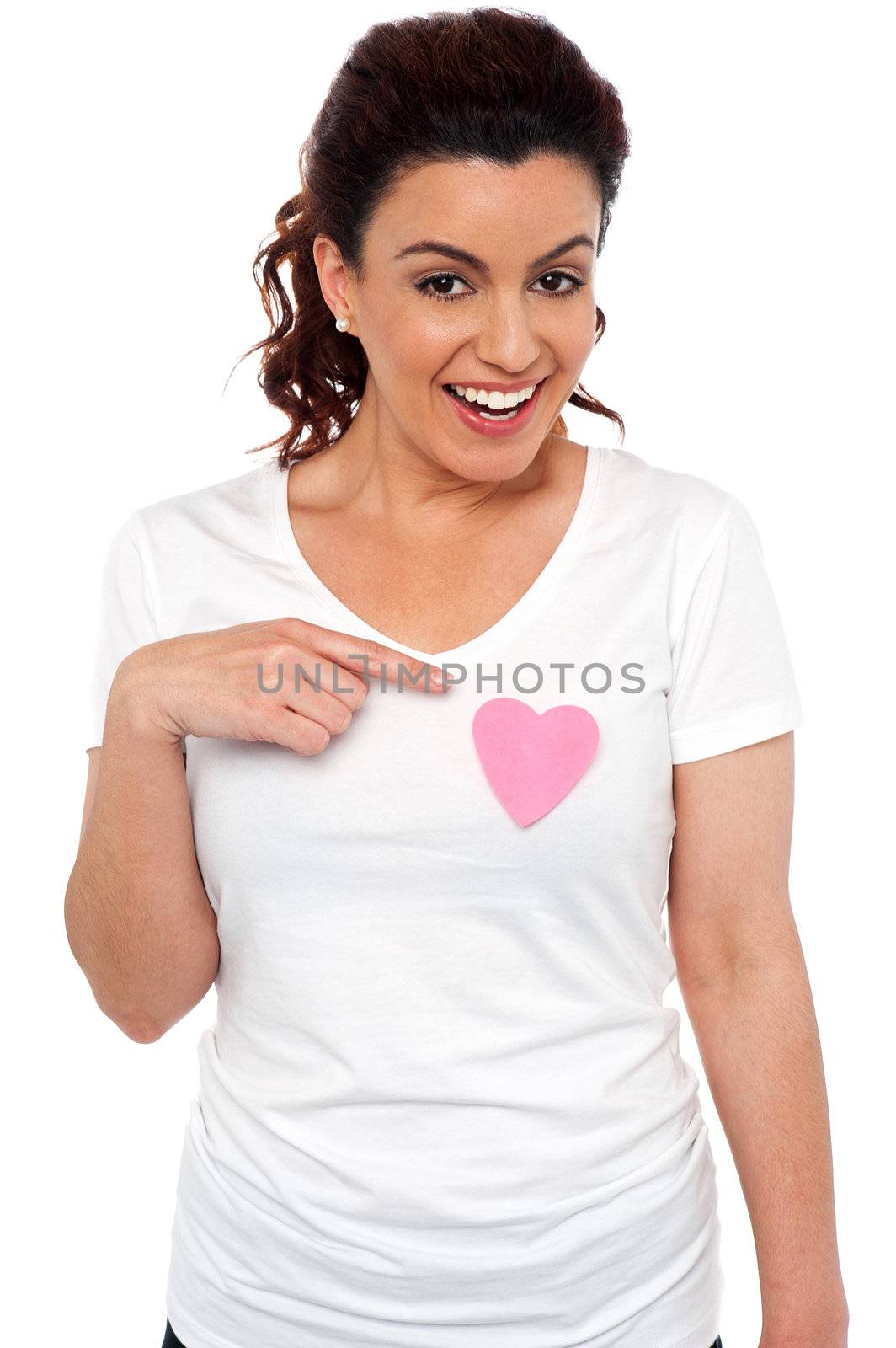 Cheerful girl pointing at pink paper heart on her t-shirt. Love concept