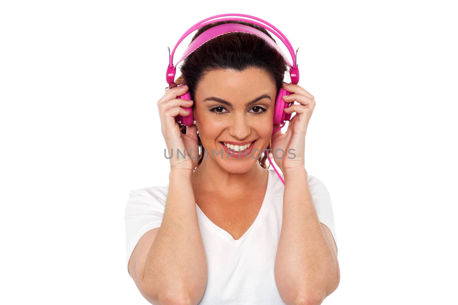 Portrait of a cheerful and charming young brunette enjoying music using pink headphones