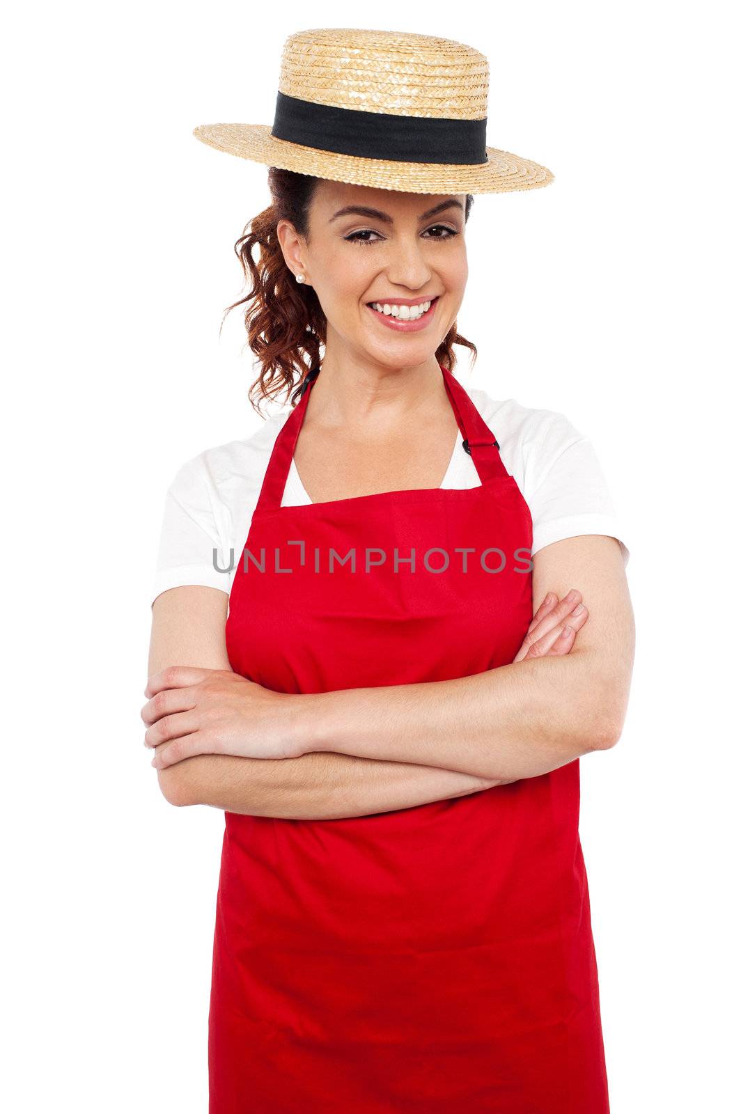 Cheerful young woman baker wearing straw bowler hat posing with her hands crossed