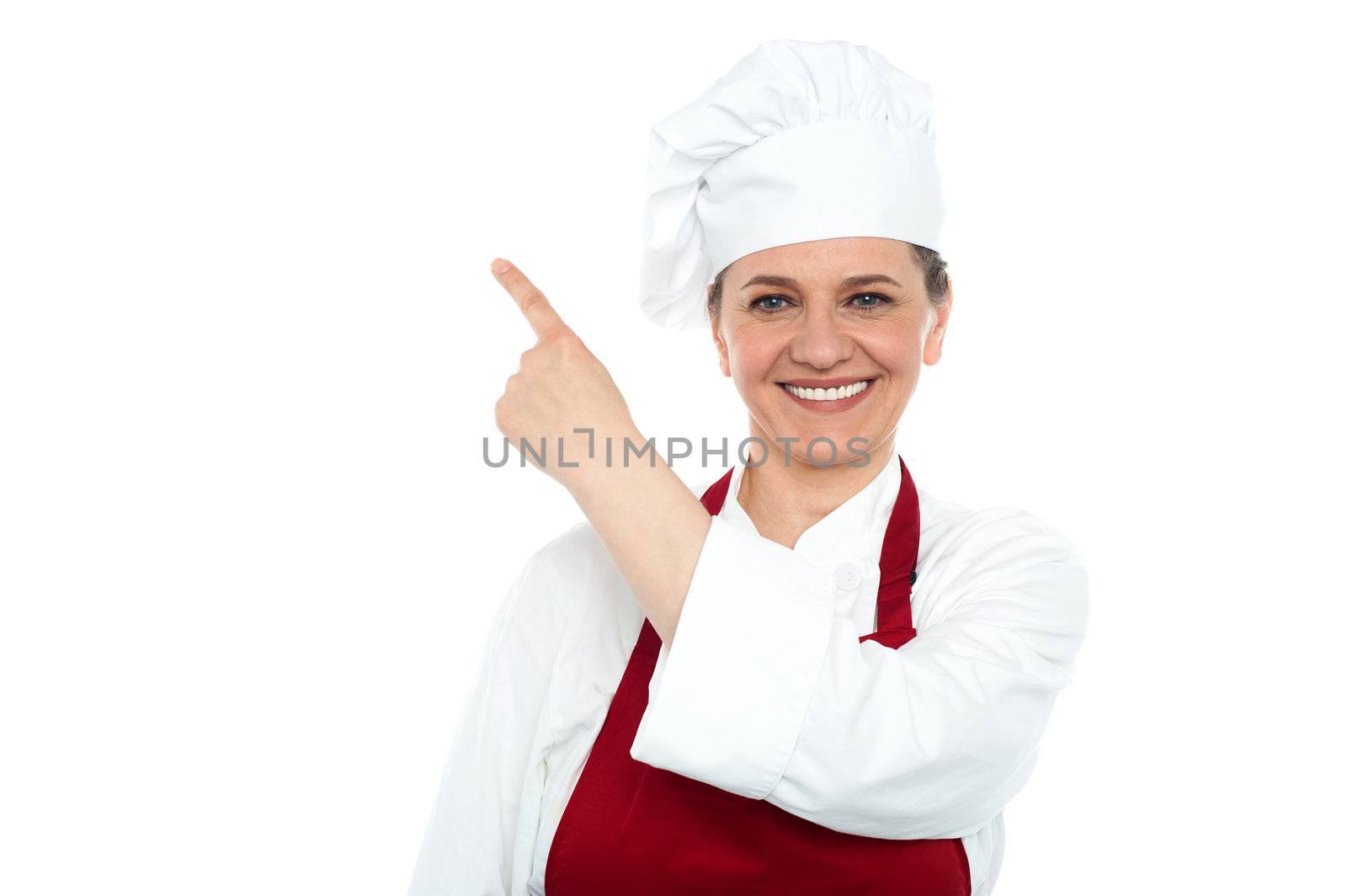 Smiling aged woman chef pointing at copy space area isolated against white background