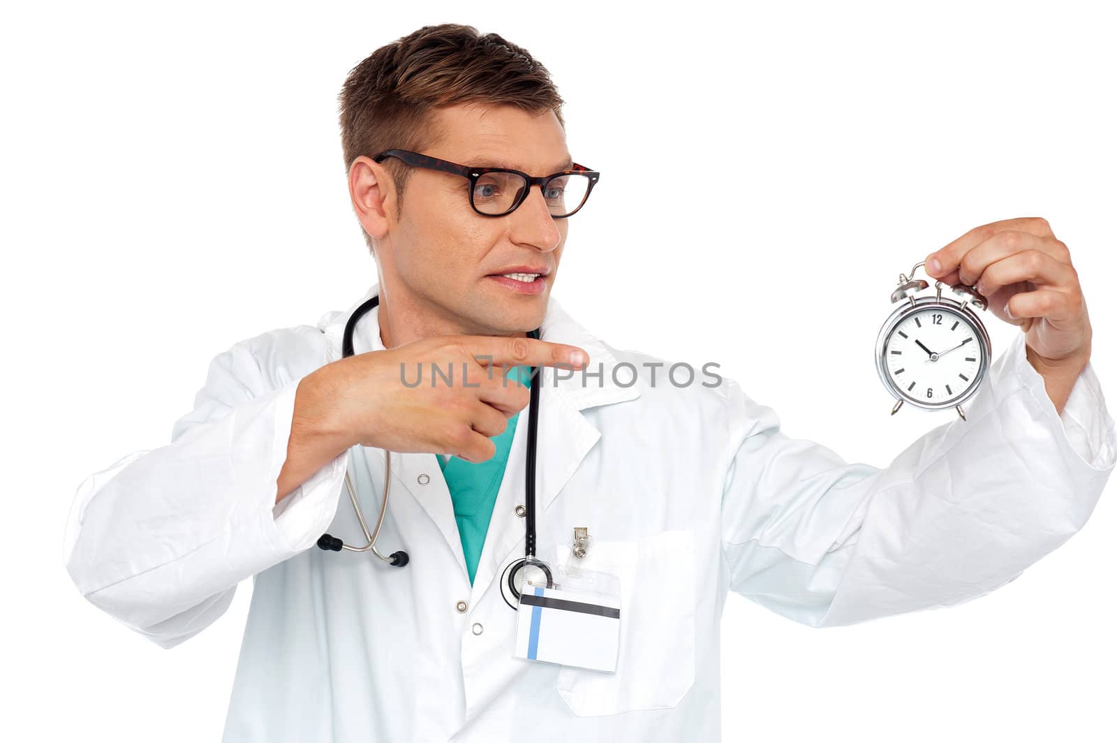 Shocking young doctor pointing at alarm clock isolated over white background