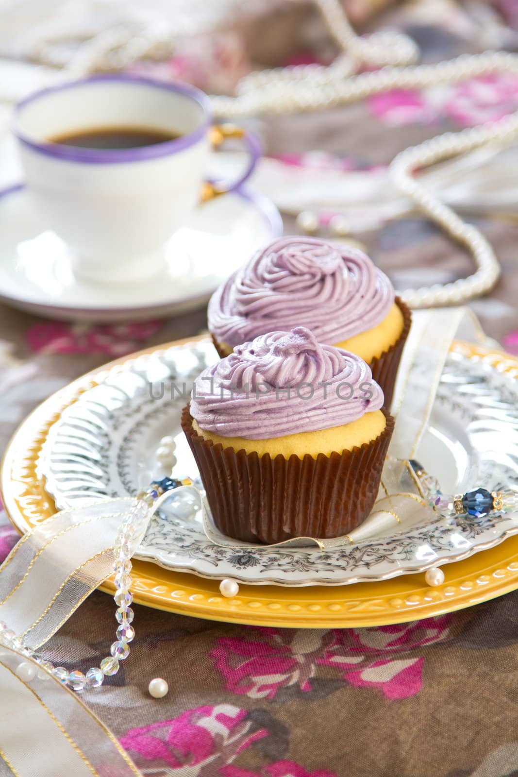 Violet cupcake with violet cream on top by coffee