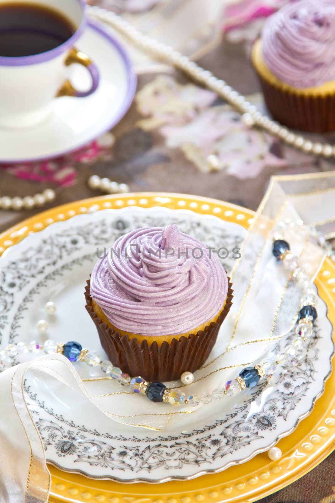 Violet cupcake with violet cream on top by coffee