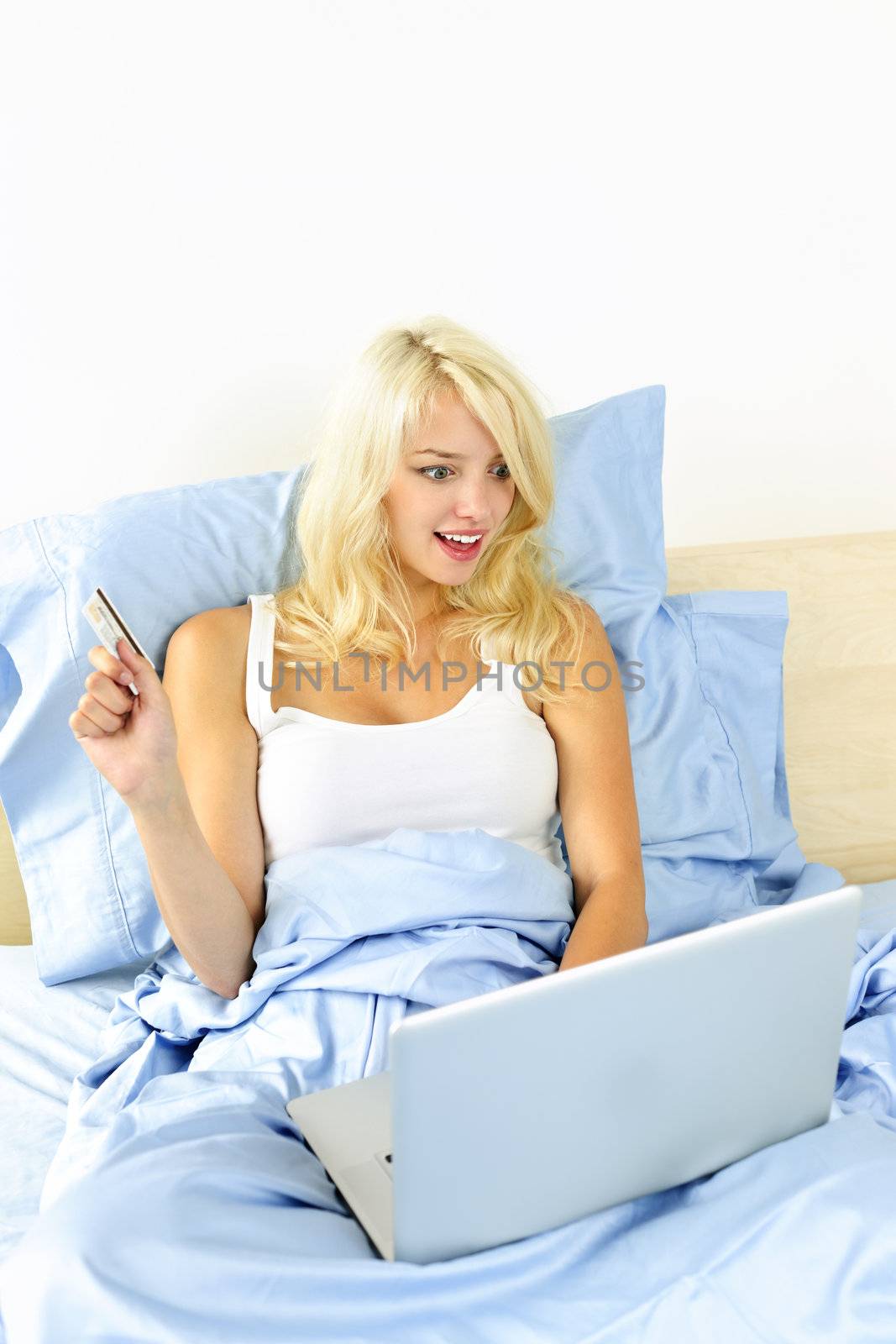 Excited blonde woman shopping online using internet in bed