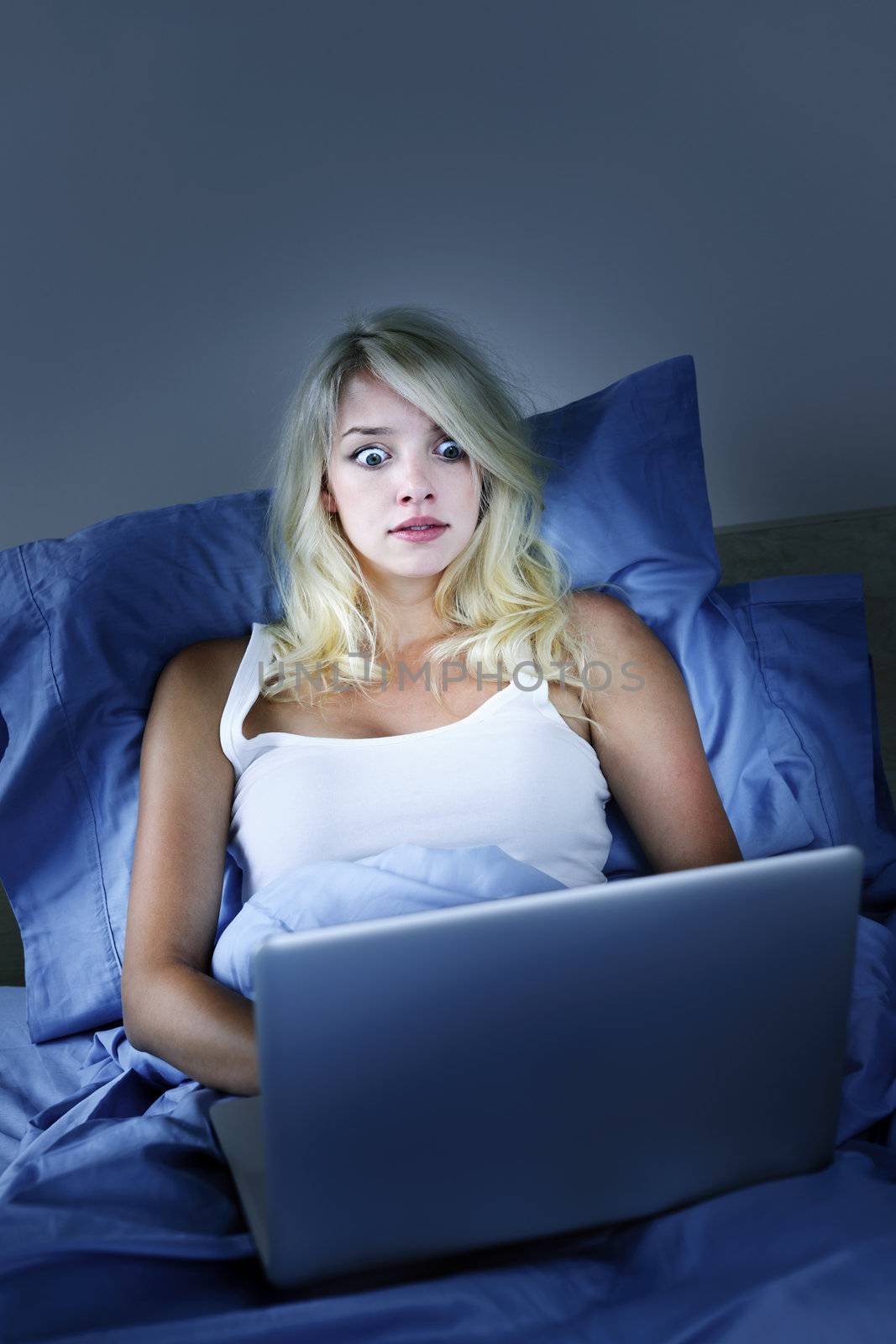 Scared woman using laptop computer in bed at night with wide eyes