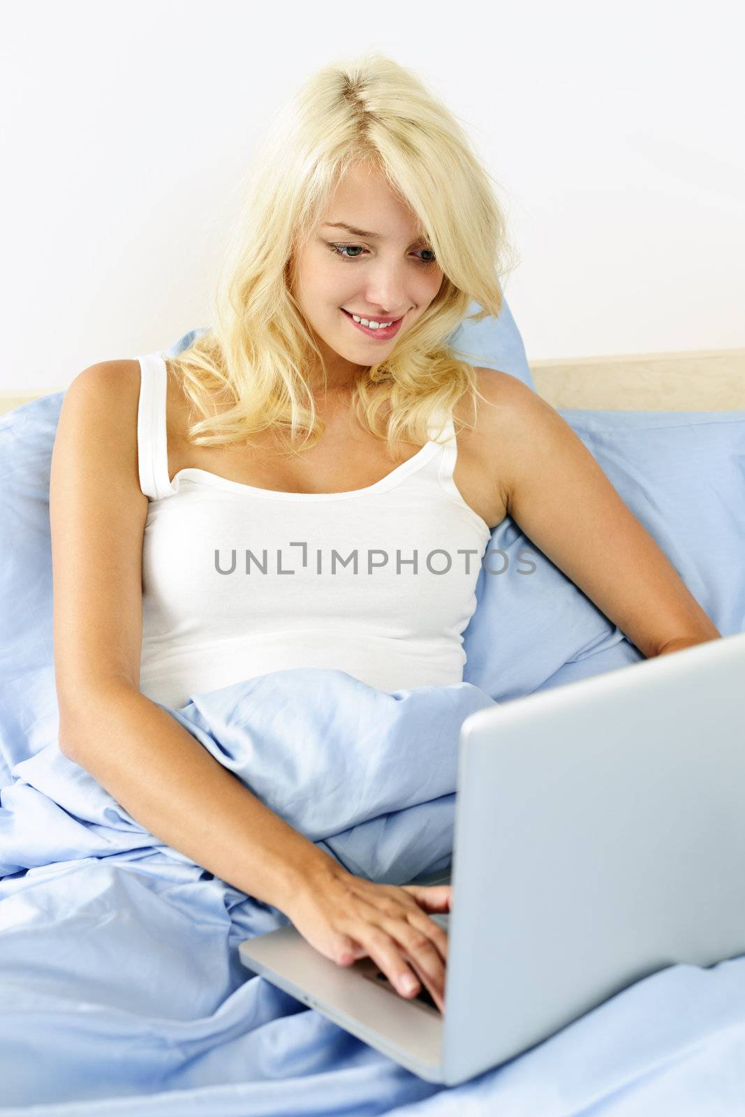 Woman sitting in bed with laptop computer by elenathewise