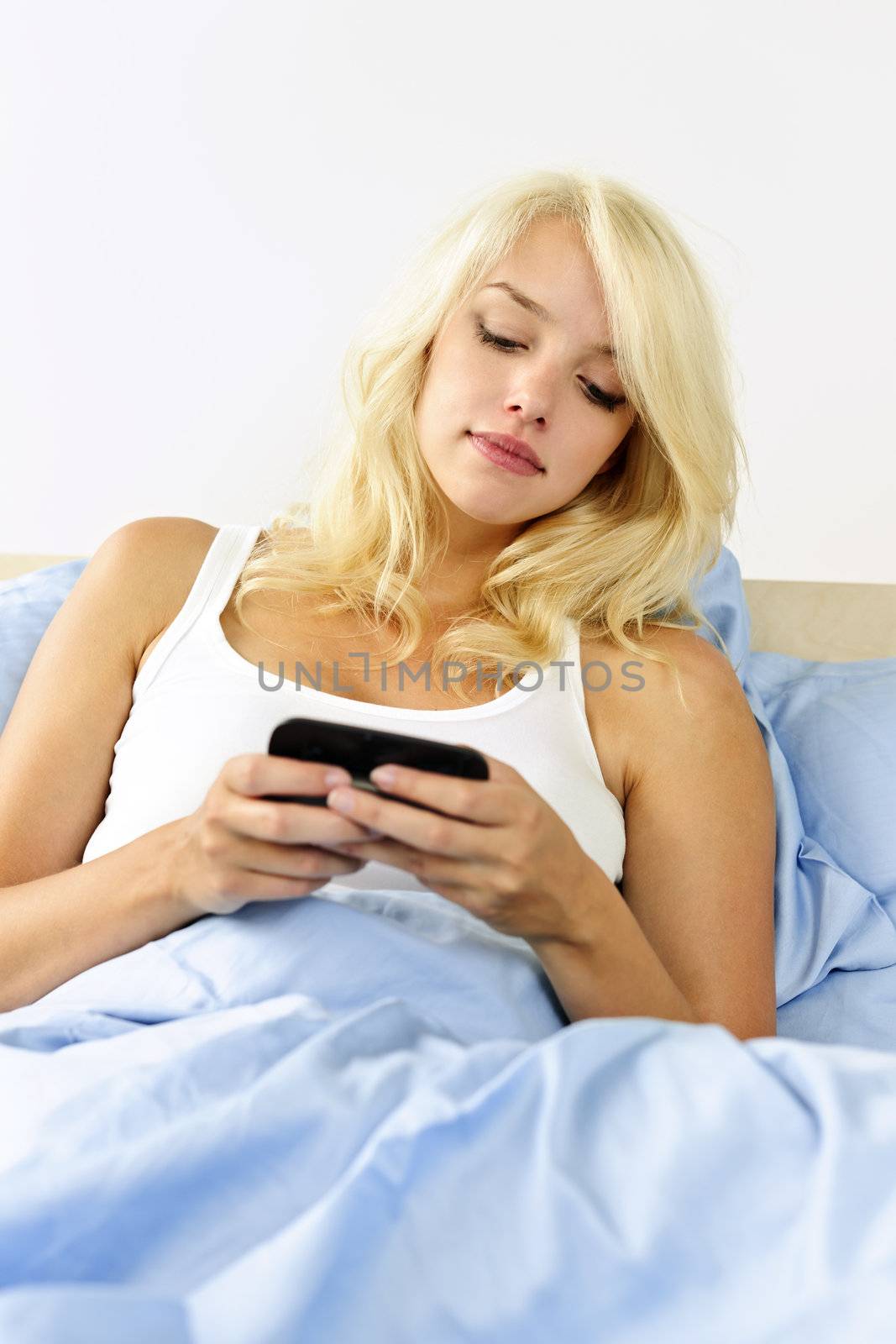 Blonde woman reading text message on phone in bed at home