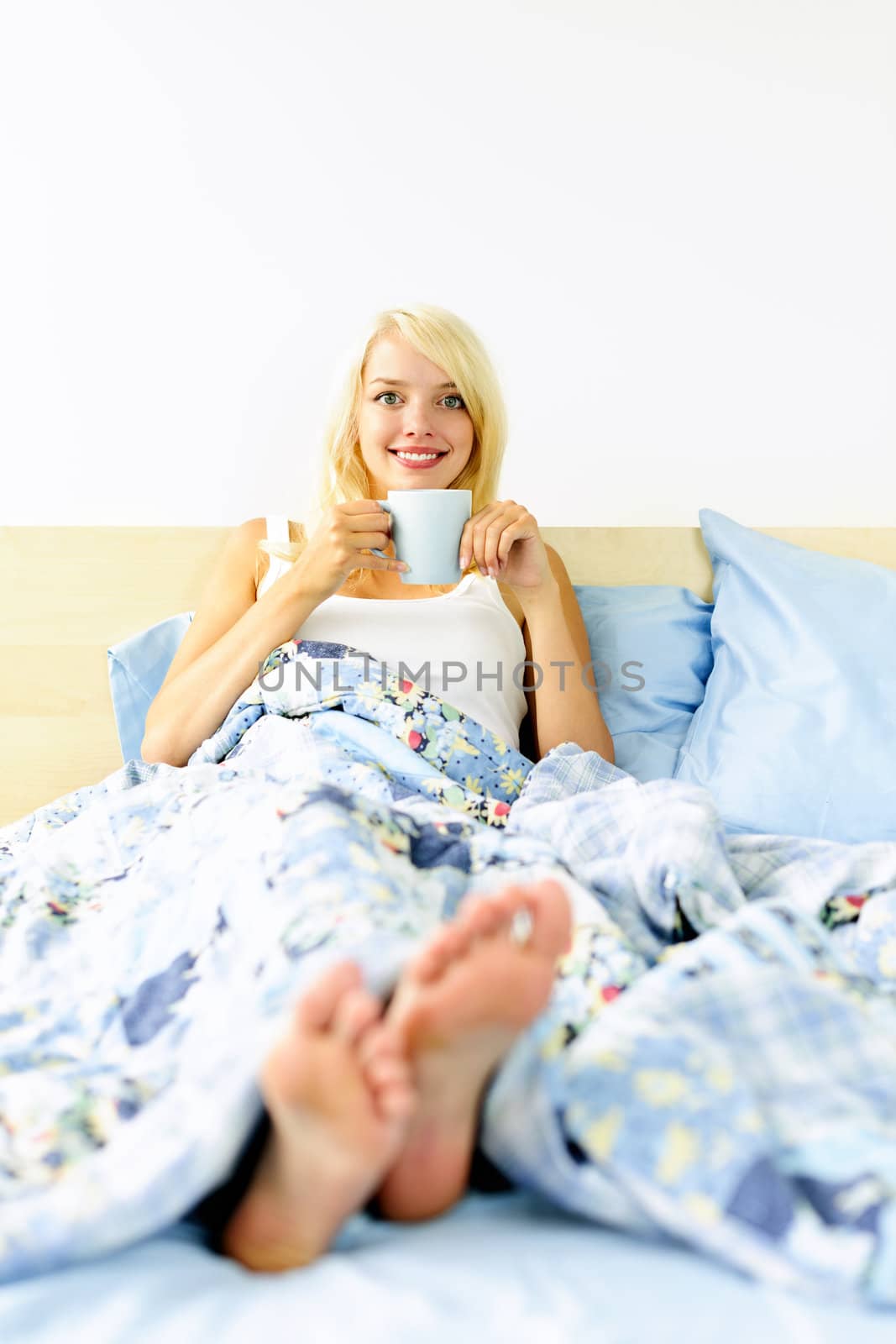 Woman sitting in bed with coffee cup by elenathewise