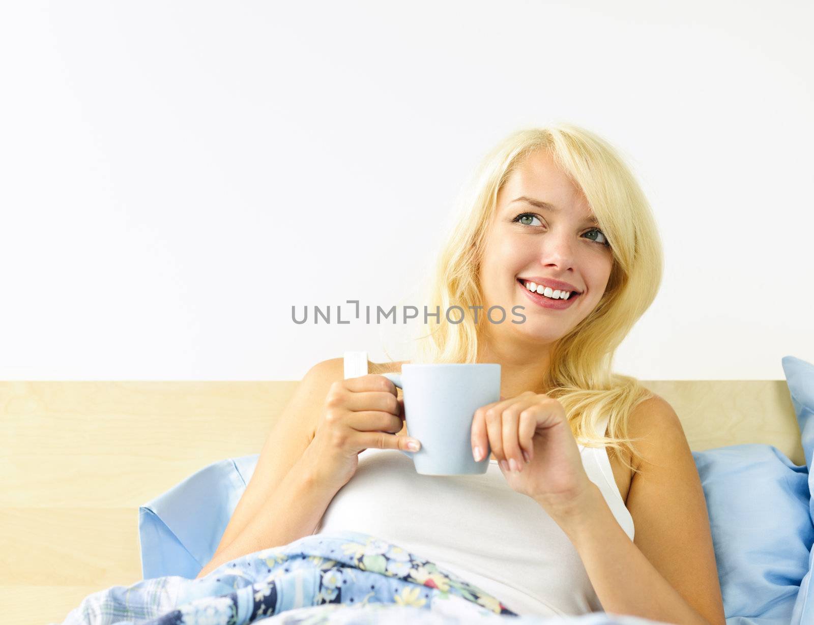 Smiling blonde woman drinking coffee and relaxing in bed in the morning