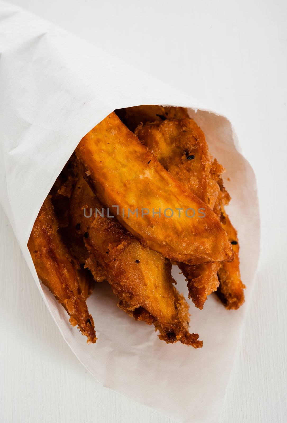 Fried sweet potatoes in a paper bag on white wooden table