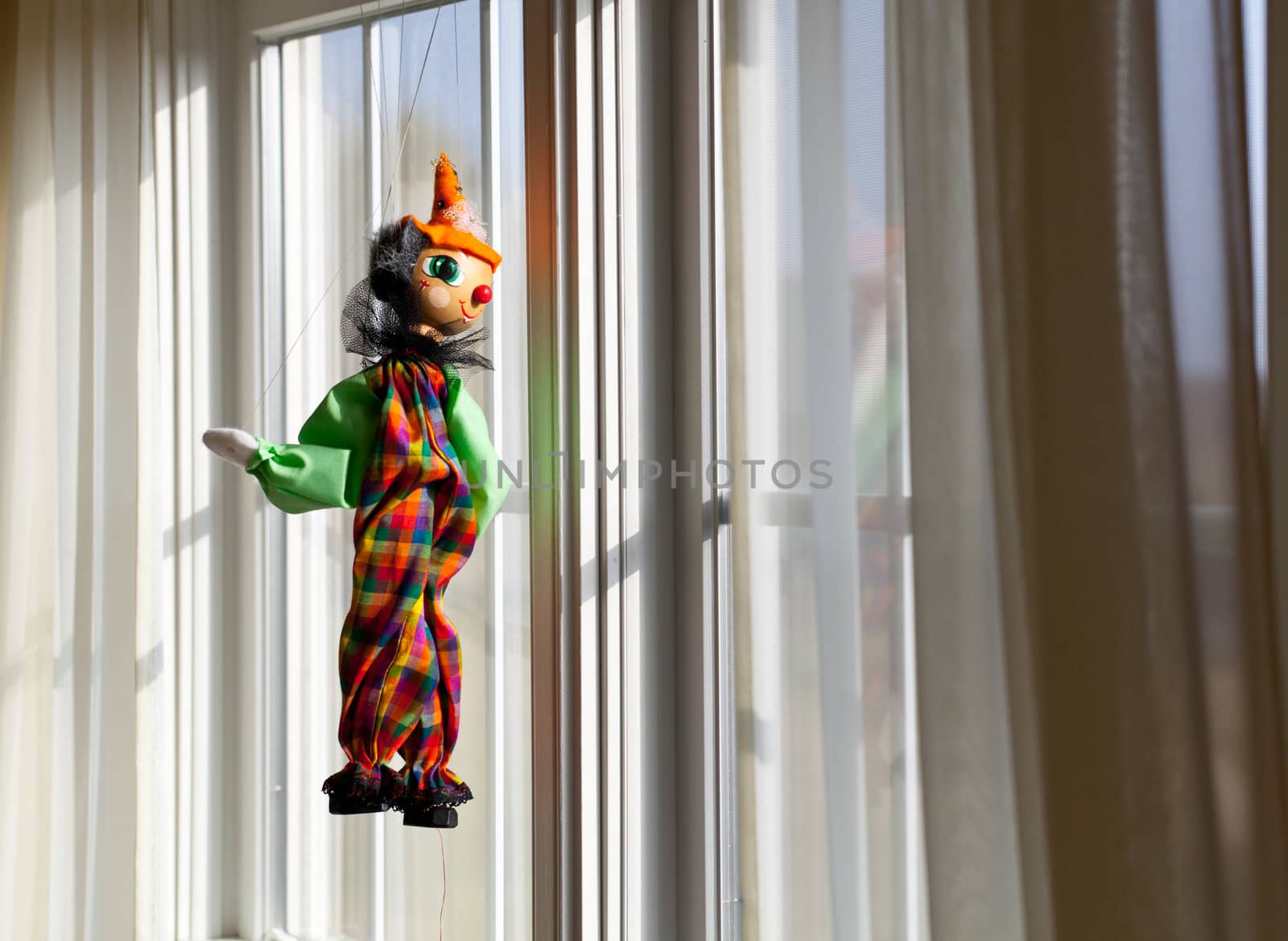 Puppet or marionette hanging in window and gazing outside into sunlit exterior