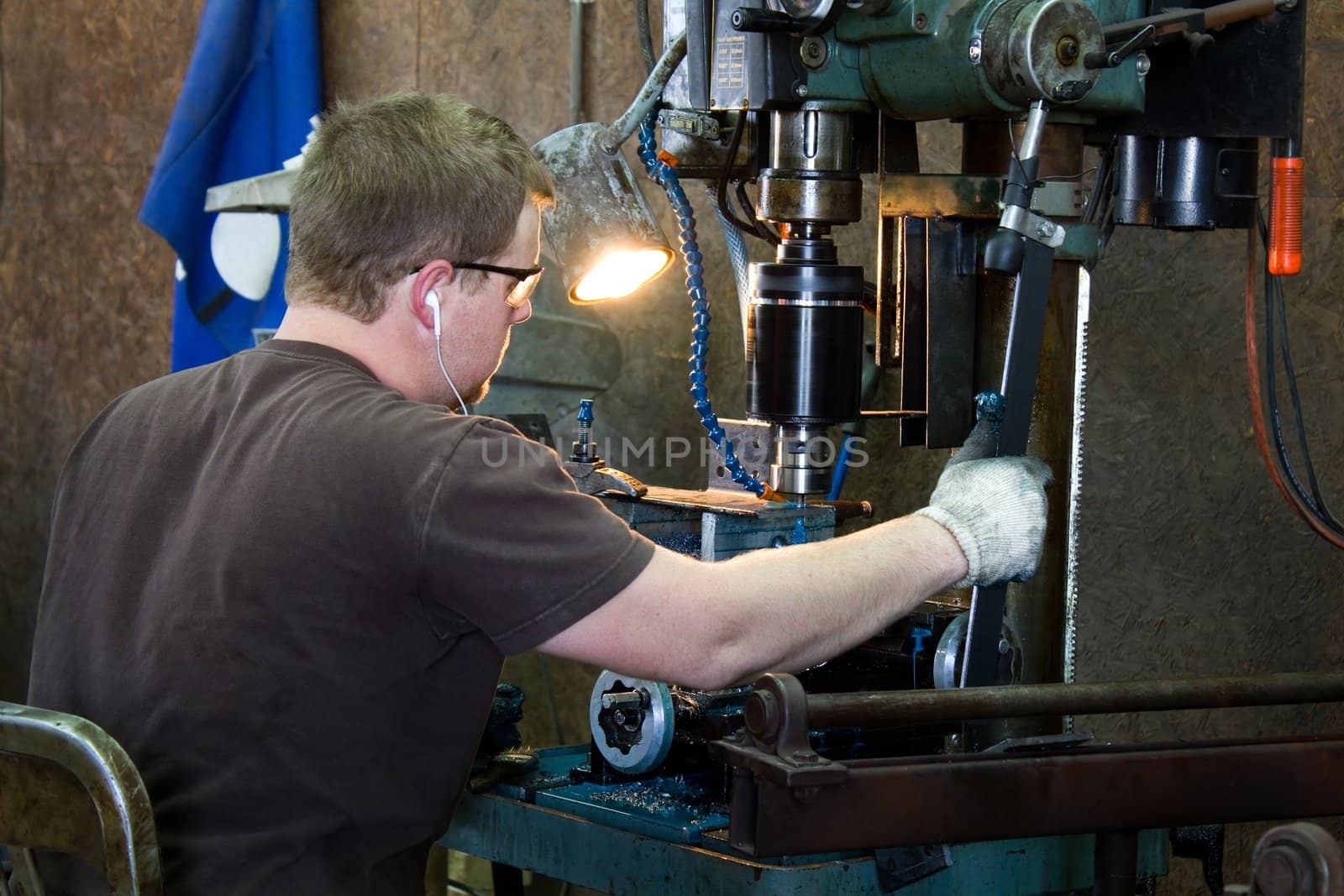 Machinist taps threads into steel using a drill press in production work in a metal shop.