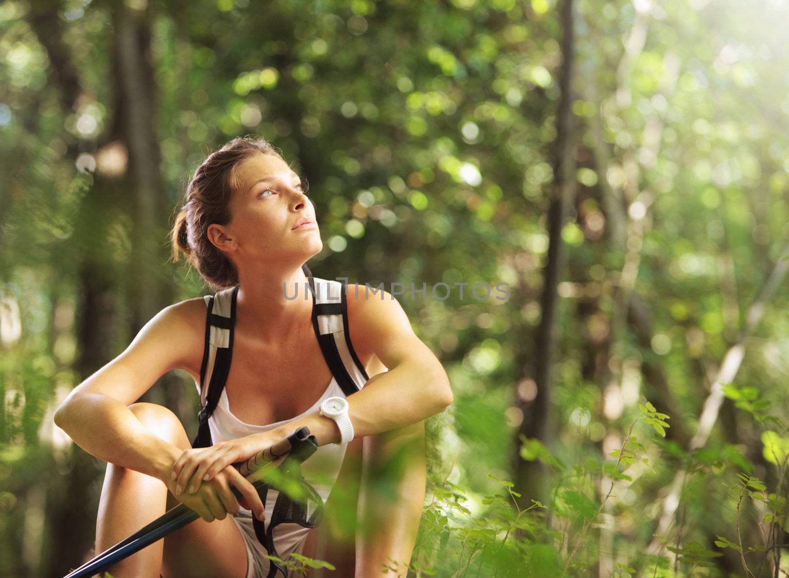 Young beautiful woman with walking sticks in a forest, having a break