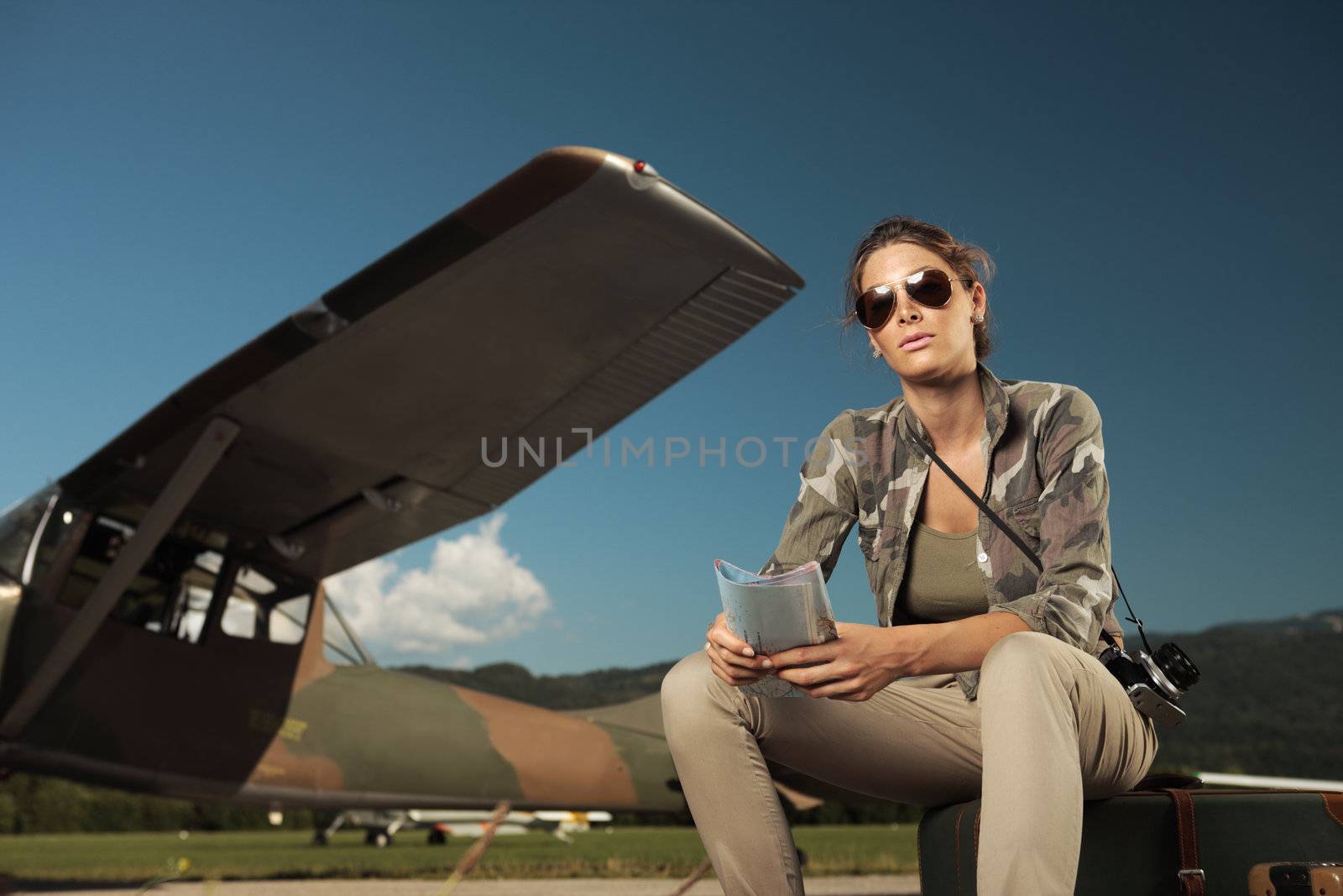 Beautiful young woman sitting on a suitcase at the airport. Airplane in the background