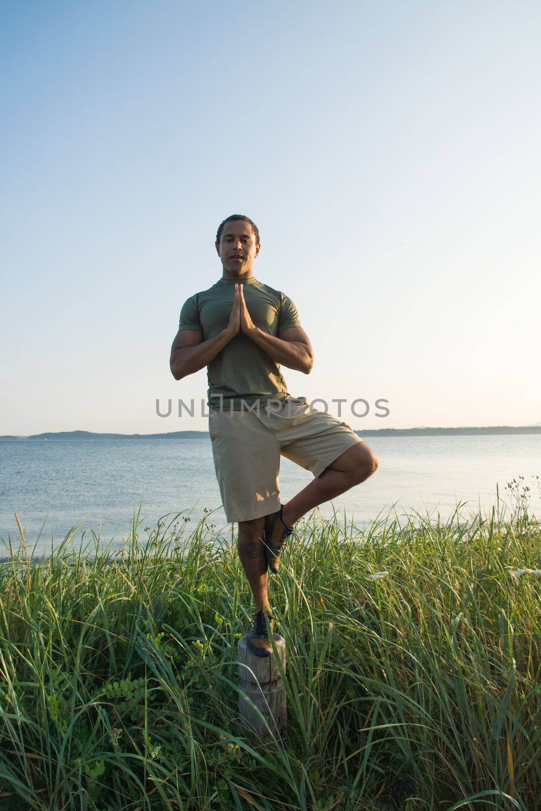 Vertical shot of young black man at beach balancing on trail post with shoreline in background.