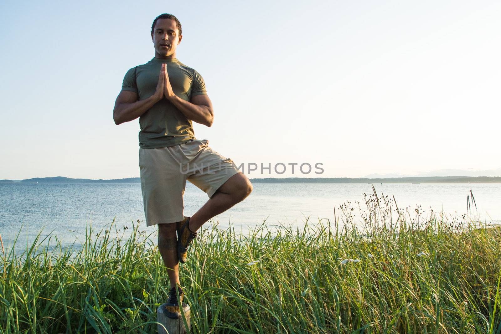 Young black man at beach balancing on trail post with shoreline in background.