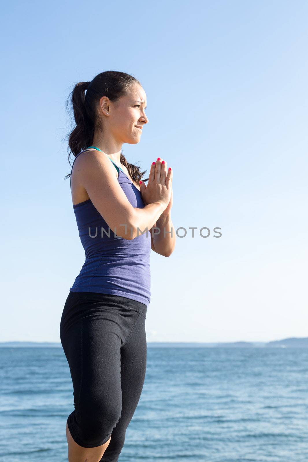 Close up of young women on beach in upright yoga pose with water in background. She is posing in the Tree pose.