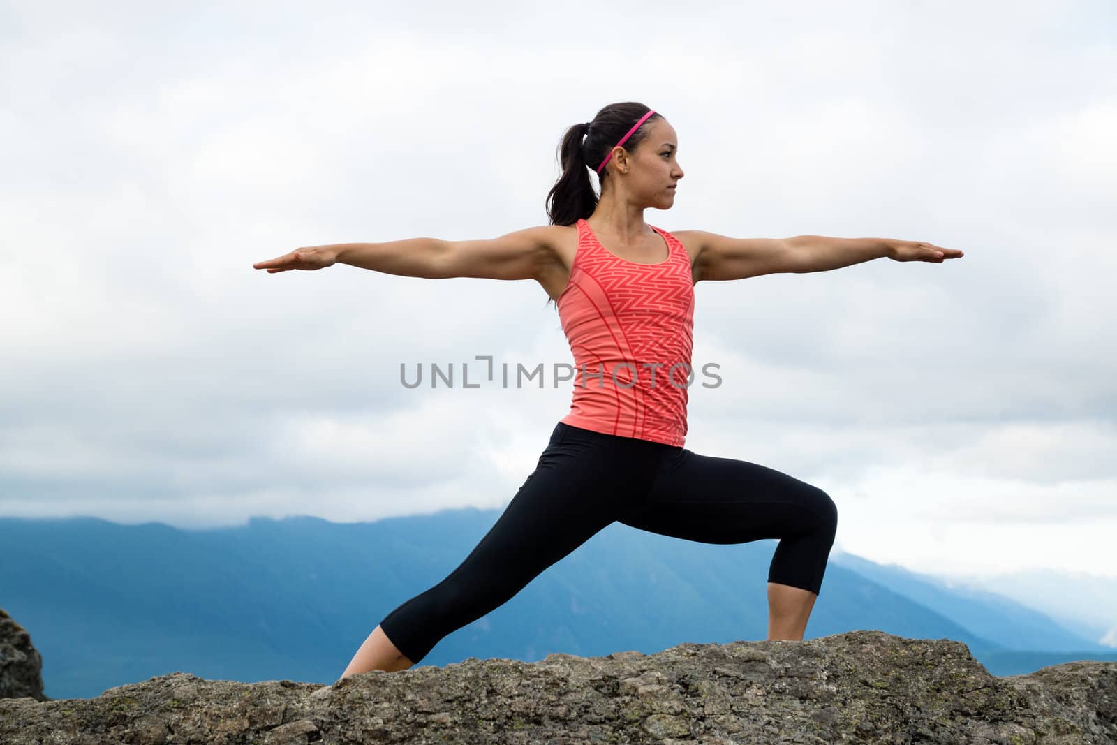 Young woman in yoga pose on top of mountain with beautiful vista in background.