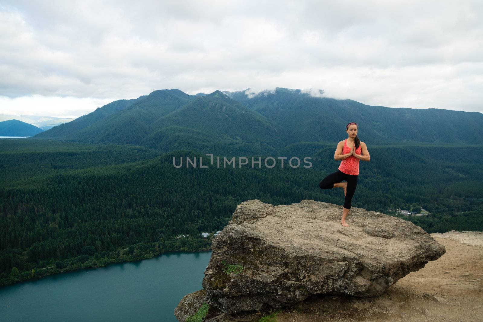 Young woman in yoga pose on top of mountain with beautiful vista in background.