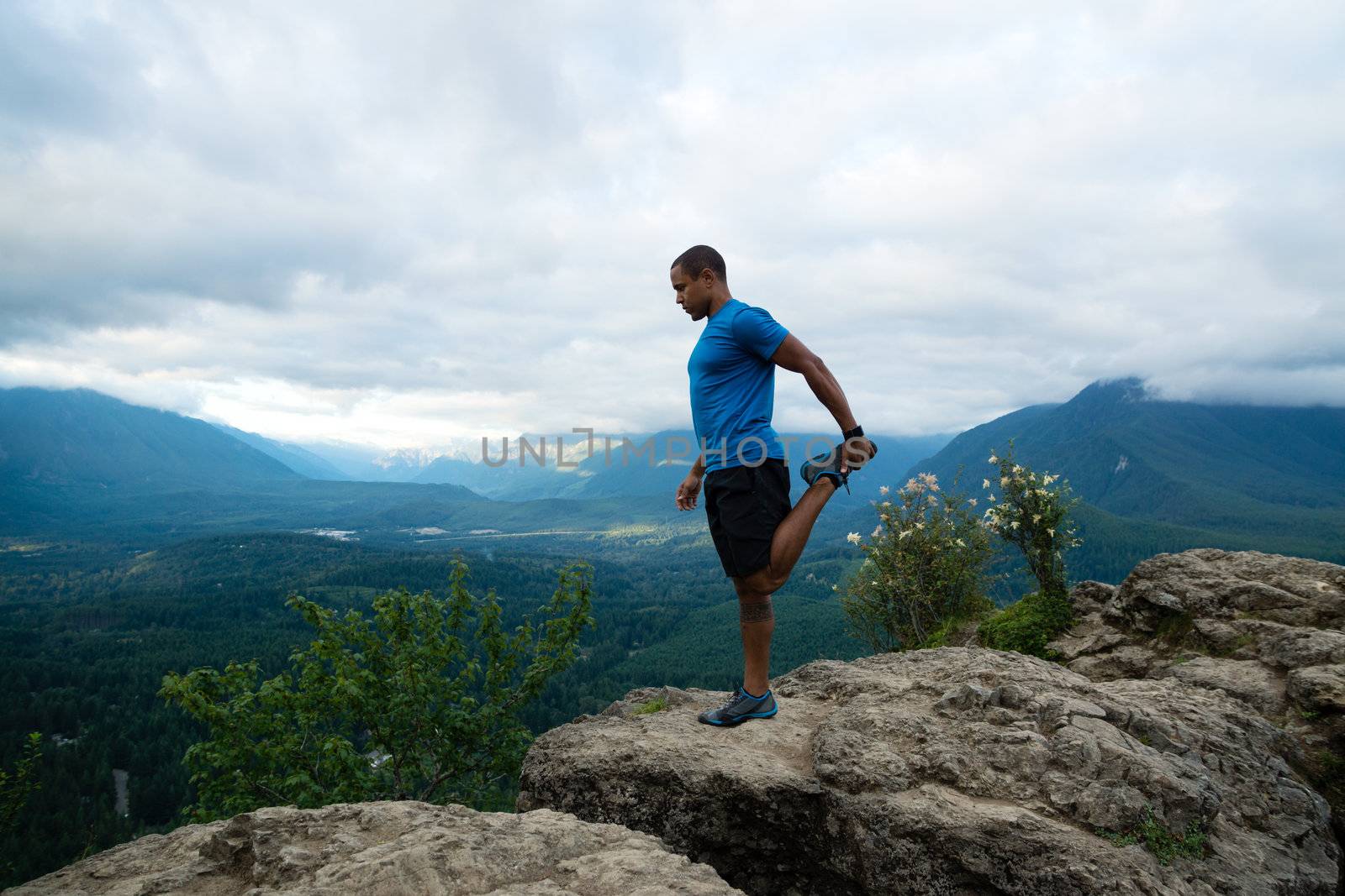 Young man in yoga pose on top of mountain with beautiful vista in background.