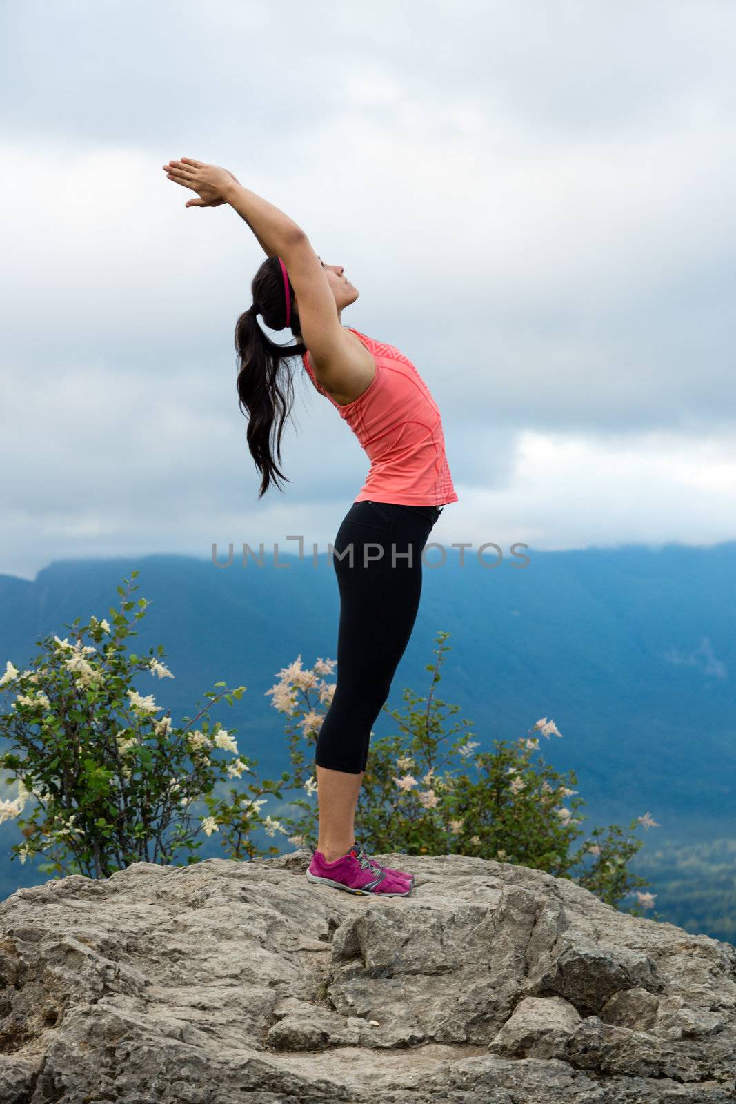 Young woman in yoga pose on top of mountain with beautiful vista in background.