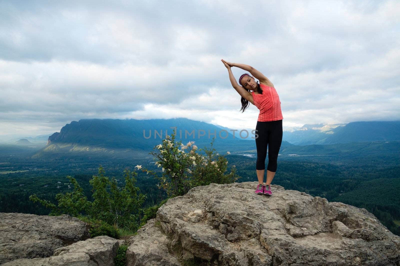 Young woman in yoga pose on top of mountain with beautiful vista in background.