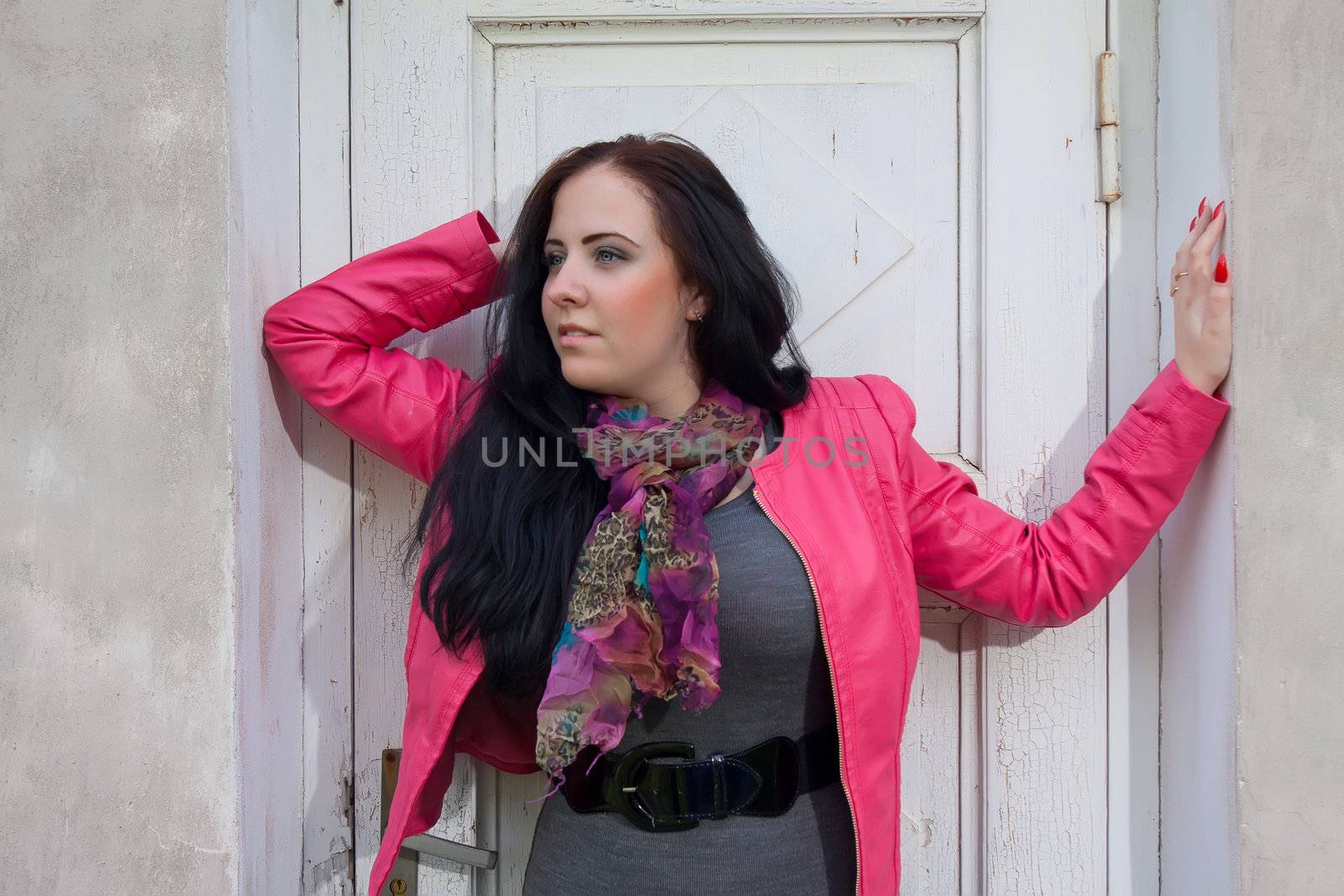 A beautiful girl looking to the side and standing in front of the closed white door.