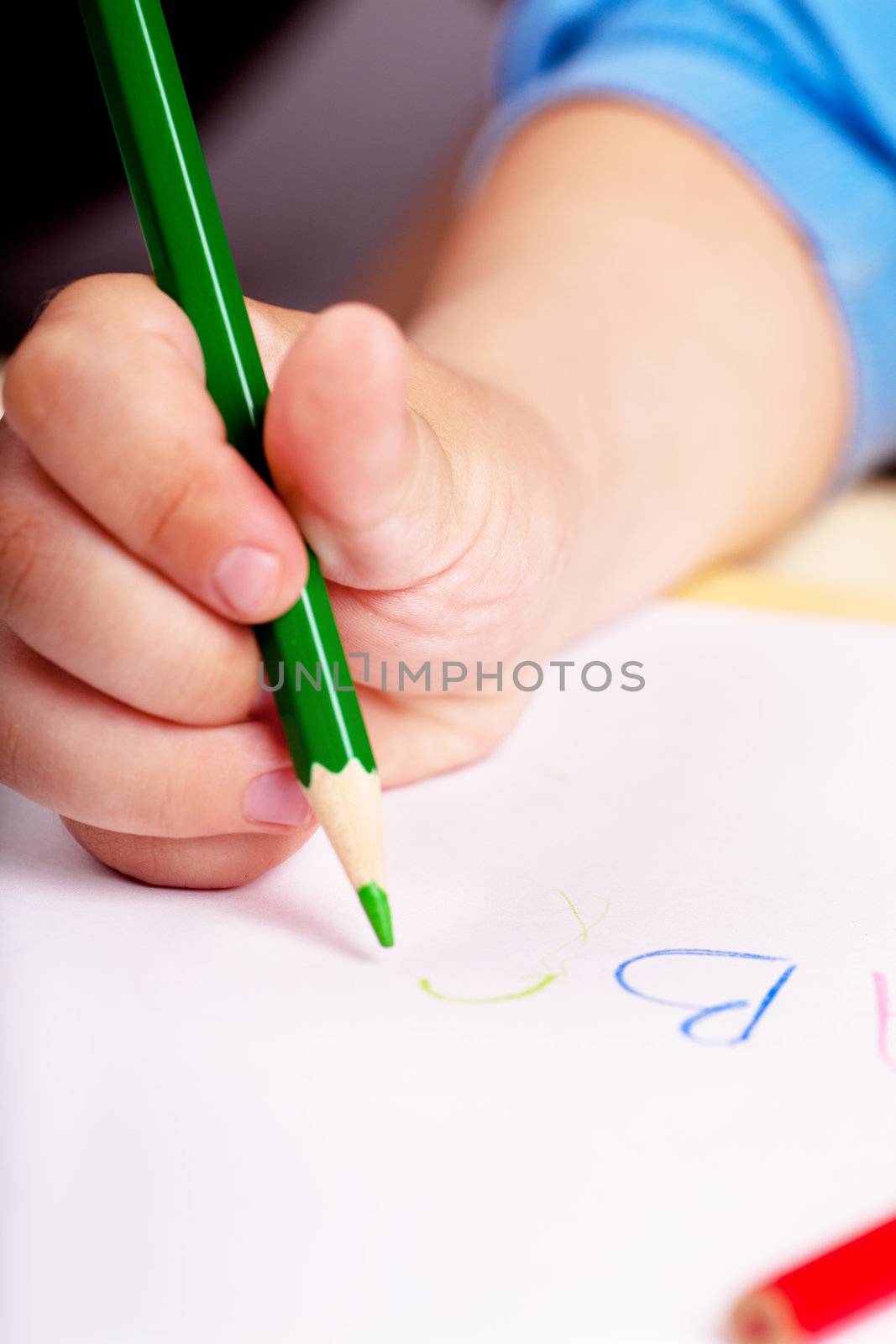 Child's hand writing letters with green pen