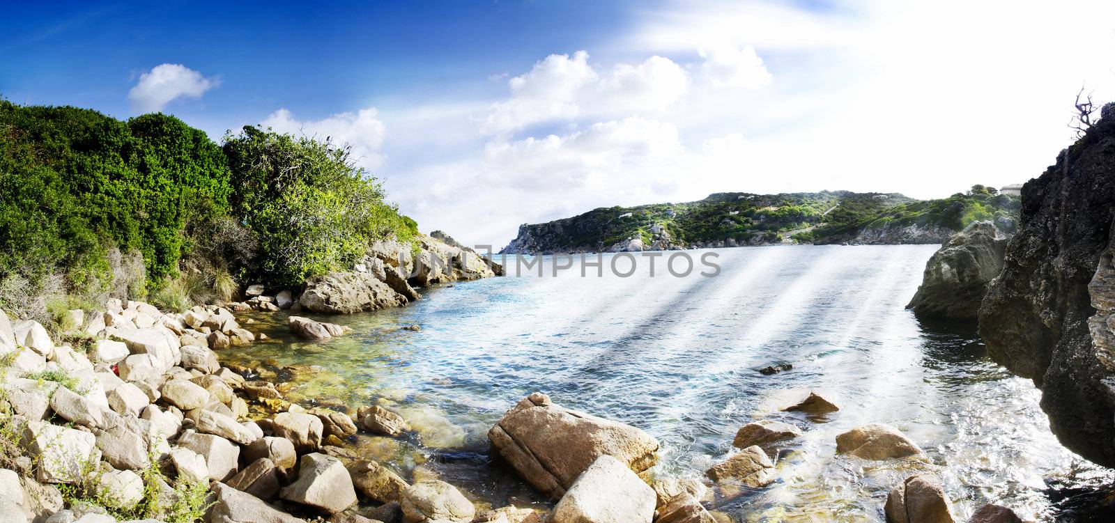Beach surrounded by rocks with a blue sky. Panorama