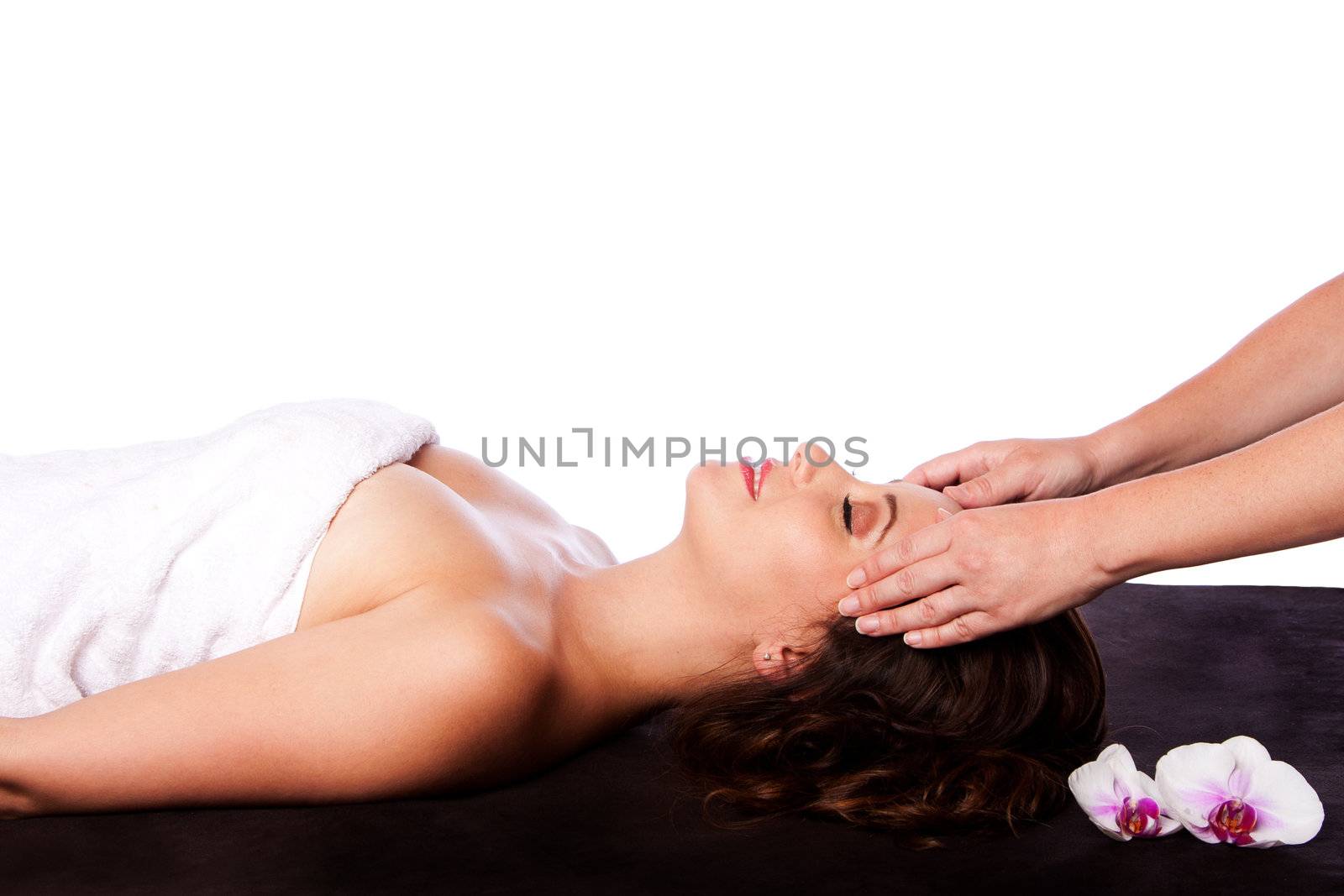 Beautiful happy peaceful sleeping woman at a spa, laying on massage table with eyes closed wearing a towel getting a facial massage, isolated.