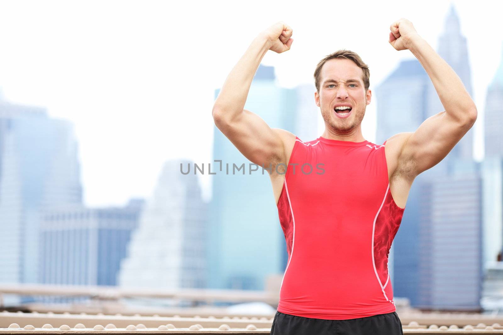 Winning athlete man celebrating flexing and showing strong muscles outside with New York City skyline in background. Young fit caucasian male fitness sports model.