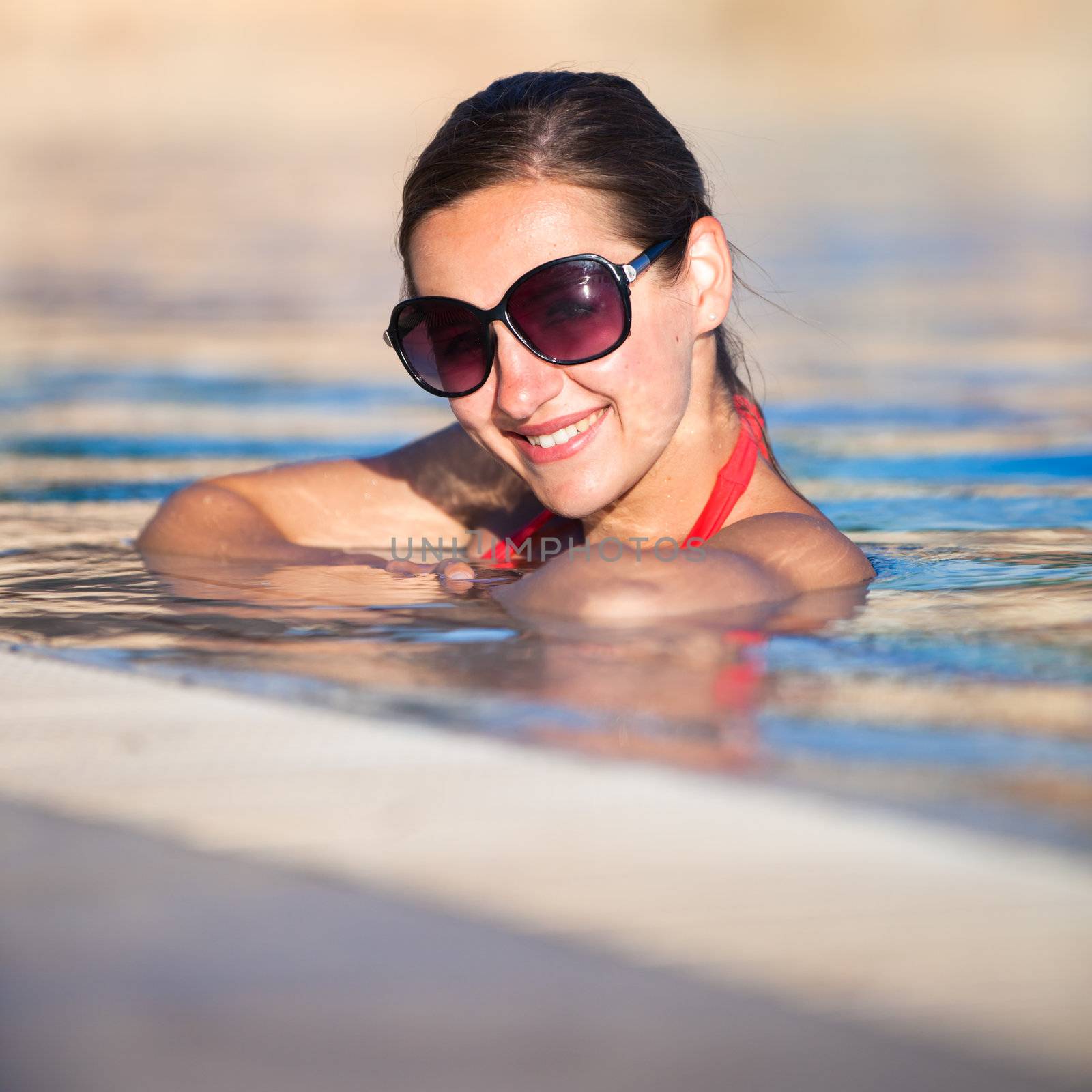 Portrait of a young woman relaxing in a swimming pool by viktor_cap